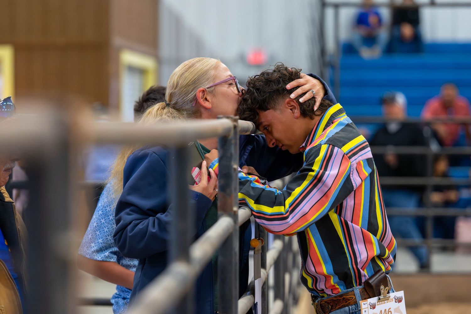 A woman kisses a child on the forehead at an indoor livestock show event.