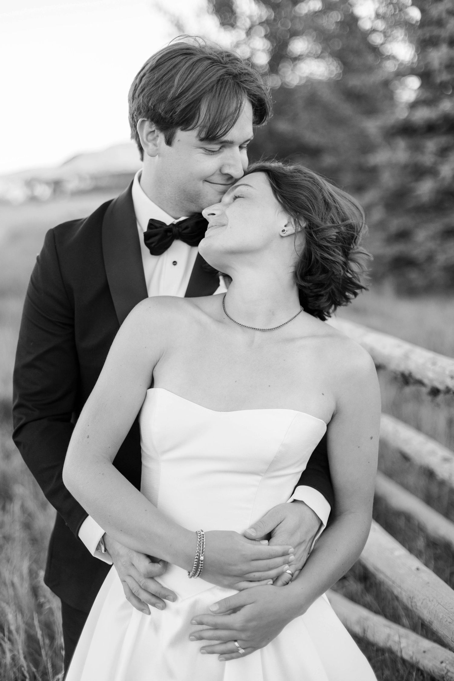 Black and white romantic wedding portrait of a couple embracing outdoors with a blurred natural background.