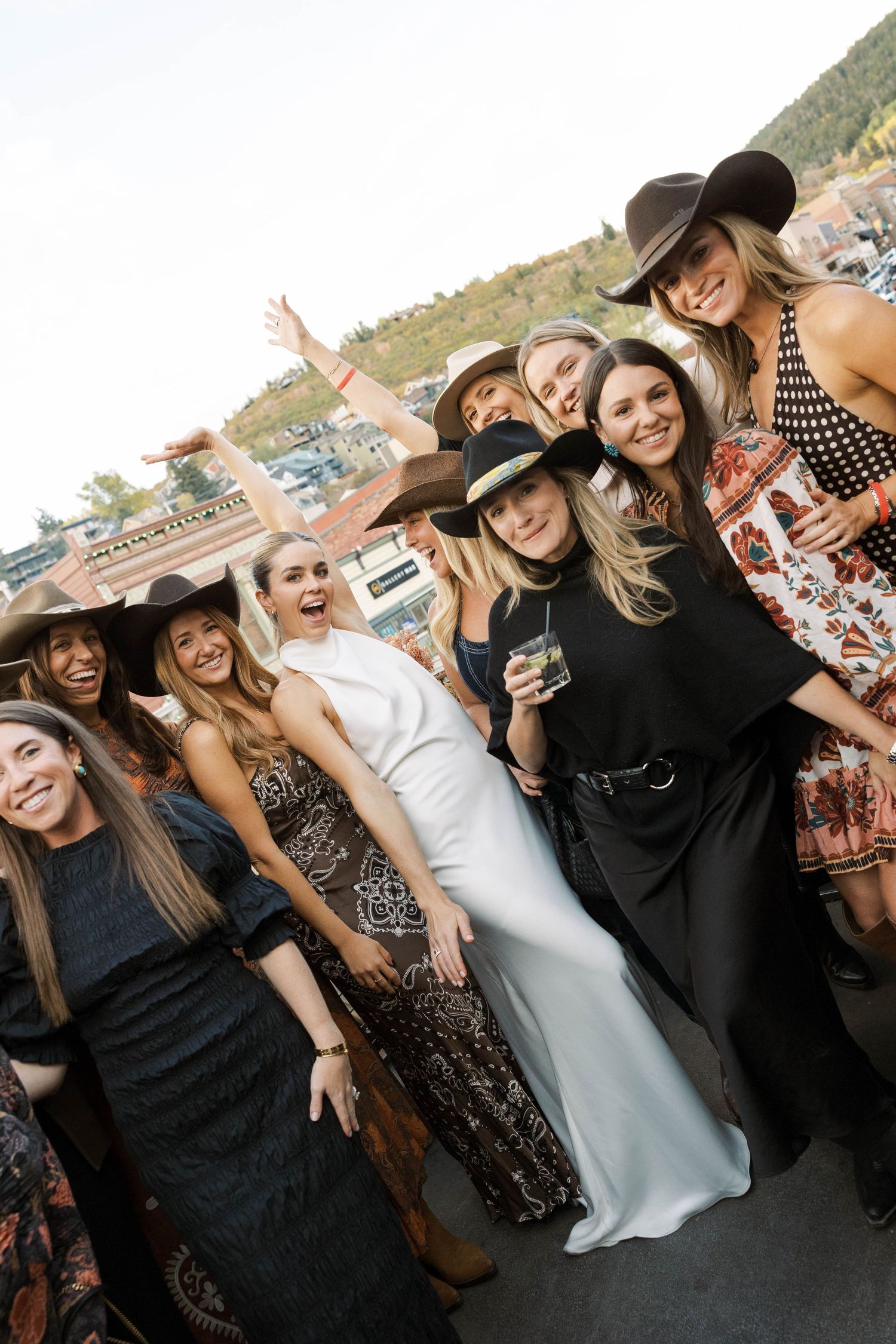 A group of friends in black dresses and cowboy hats pose together at an outdoor event.