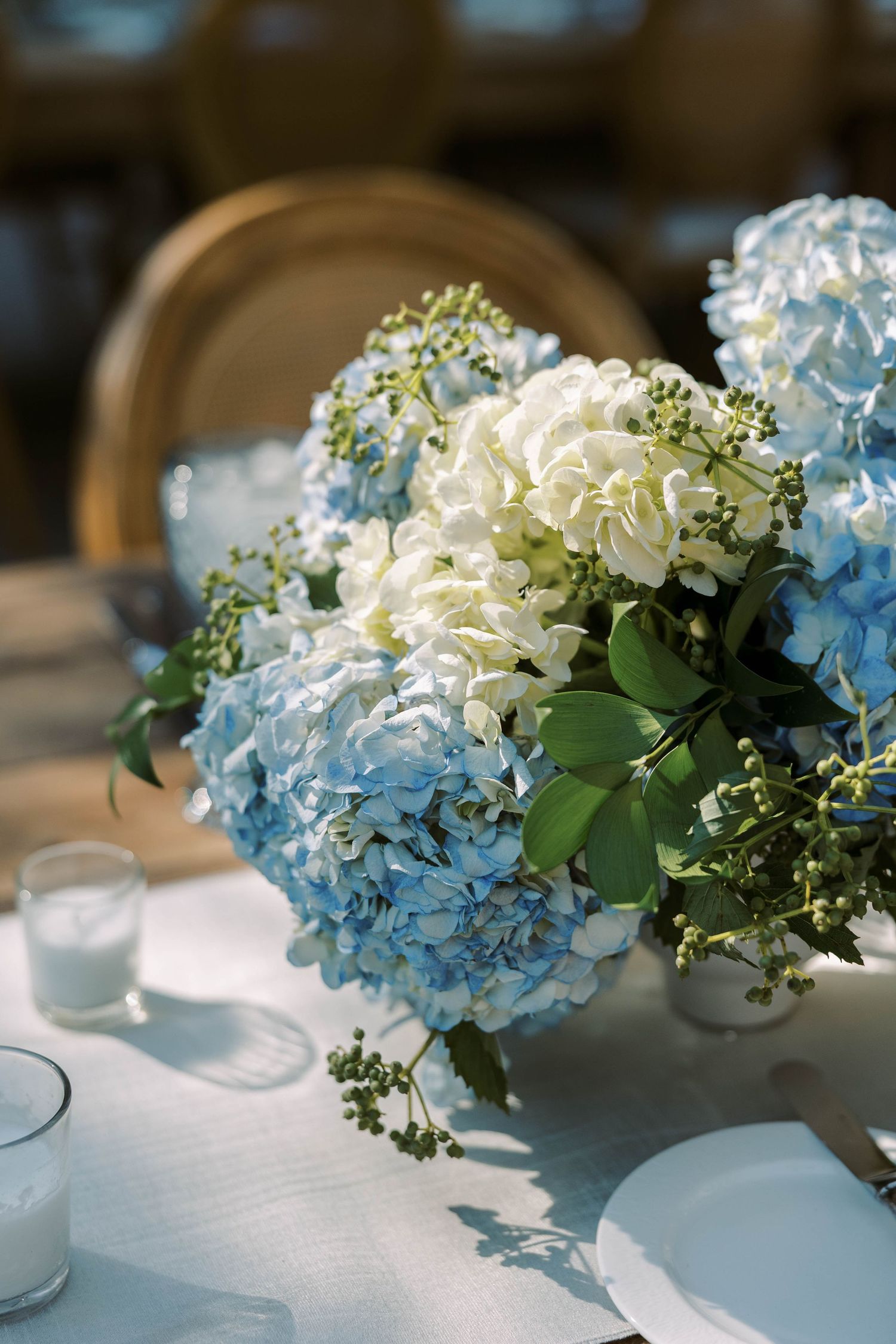 Light blue and white hydrangea flower centerpieces arranged in glass vases on a white tablecloth for an elegant event.