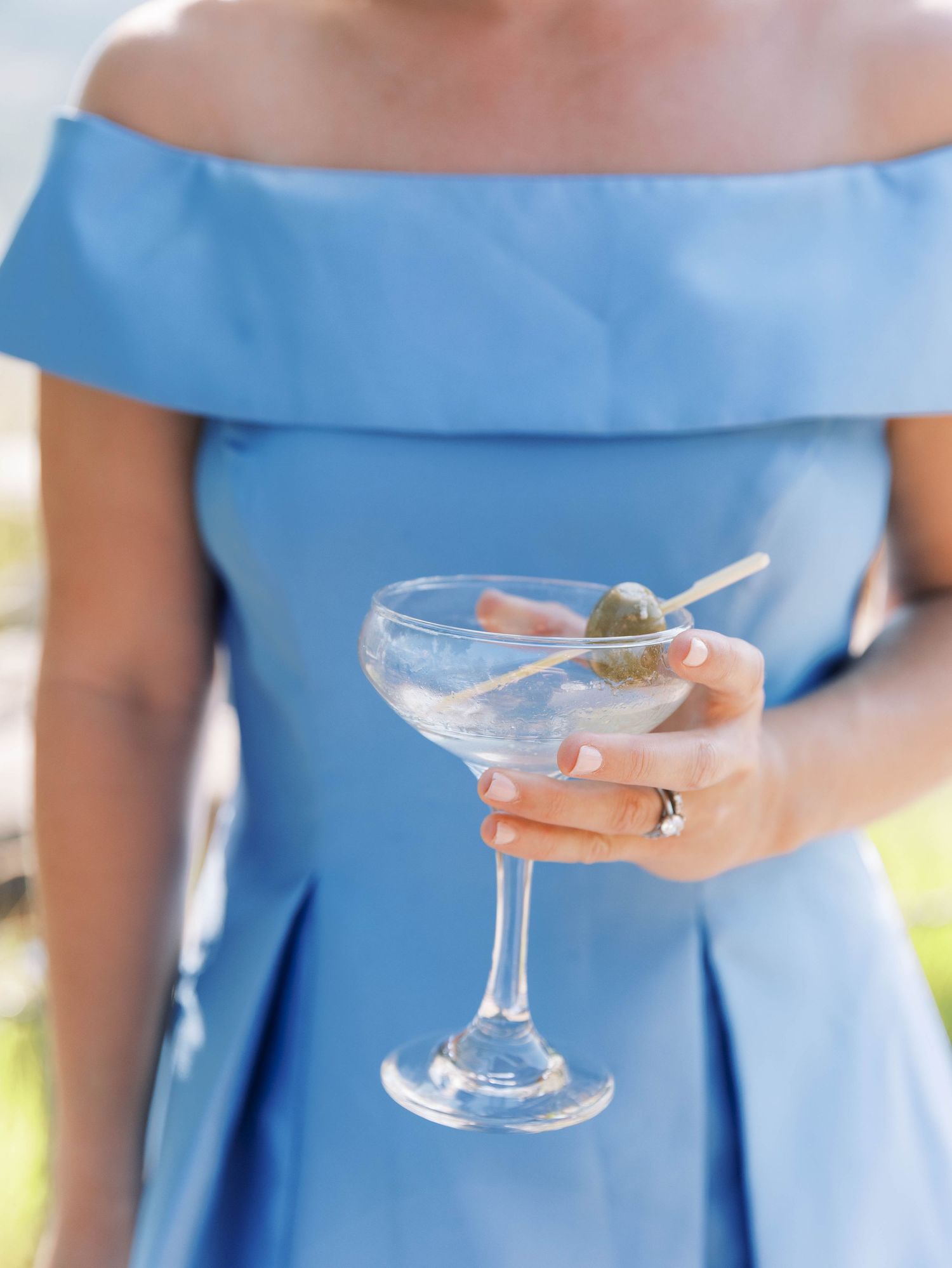 Person wearing light blue dress holding vintage coupe champagne glasses at outdoor event.