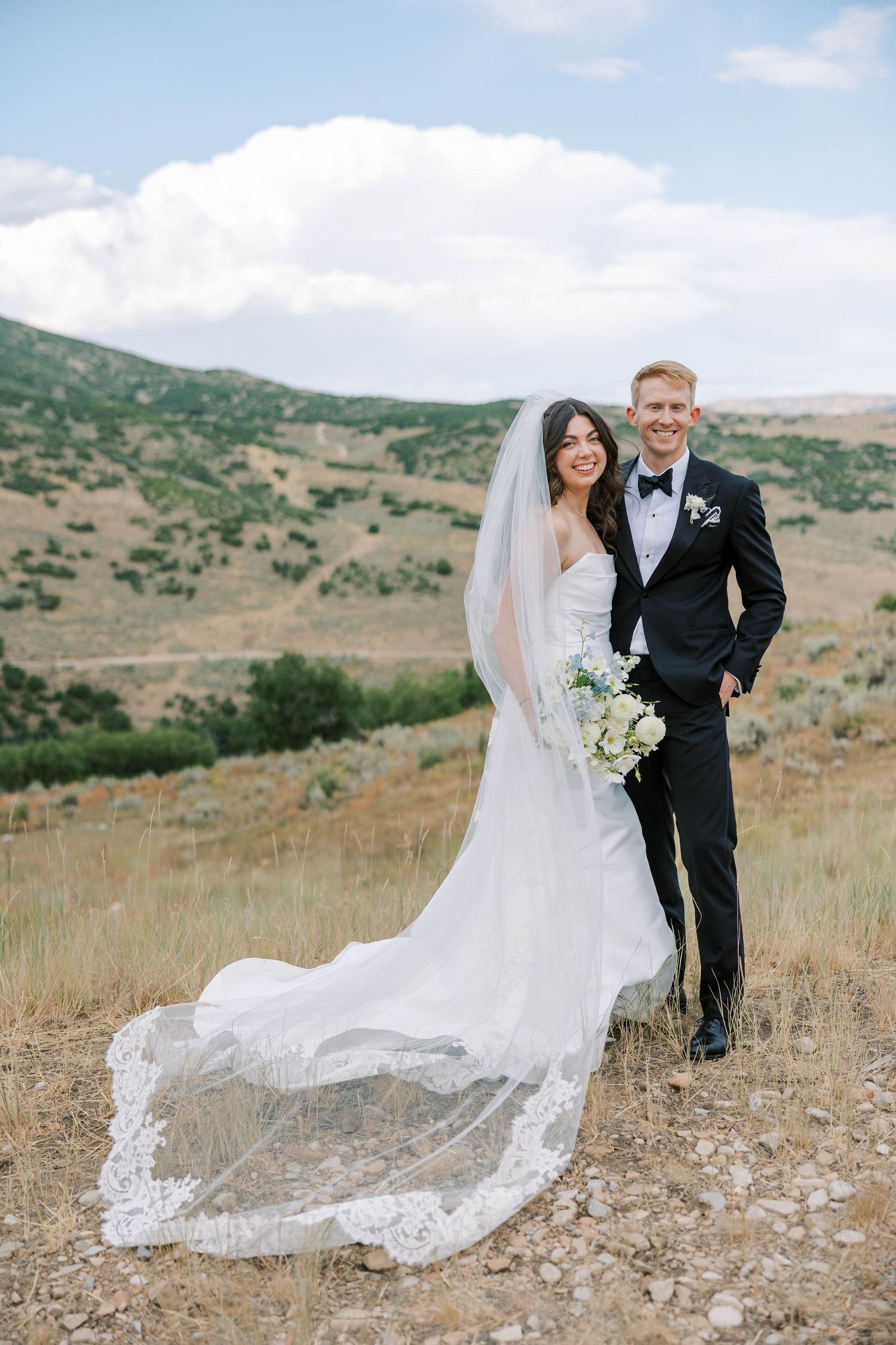 Wedding couple posing in a scenic mountain landscape with flowing veil catching the wind.