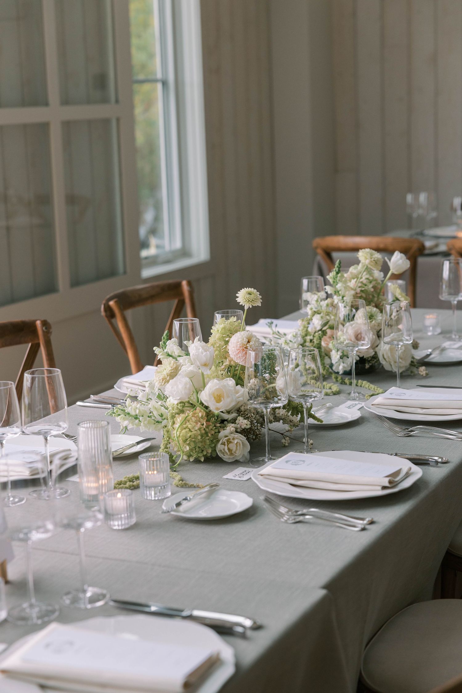 Elegant table setting with white floral centerpieces and gray linens in a bright dining room with natural light.