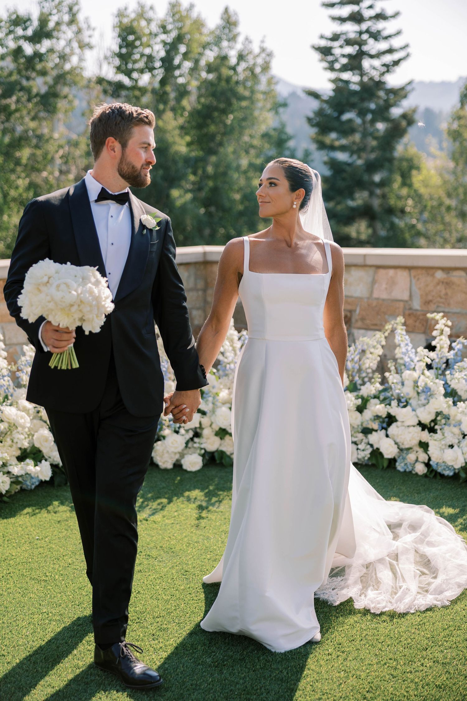 Elegant bride and groom share romantic moments in outdoor garden setting with mountain views and white floral decor.