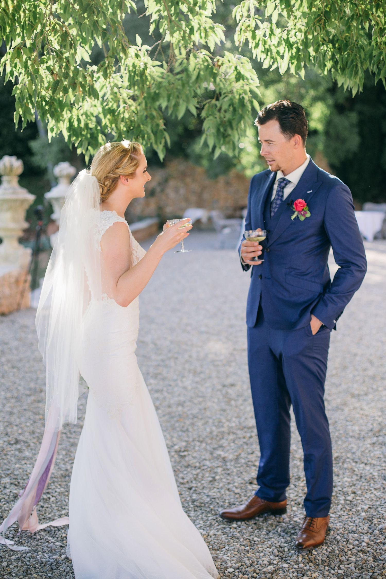 Candid moment between newlyweds on gravel path under green trees at chateau de moissac.
