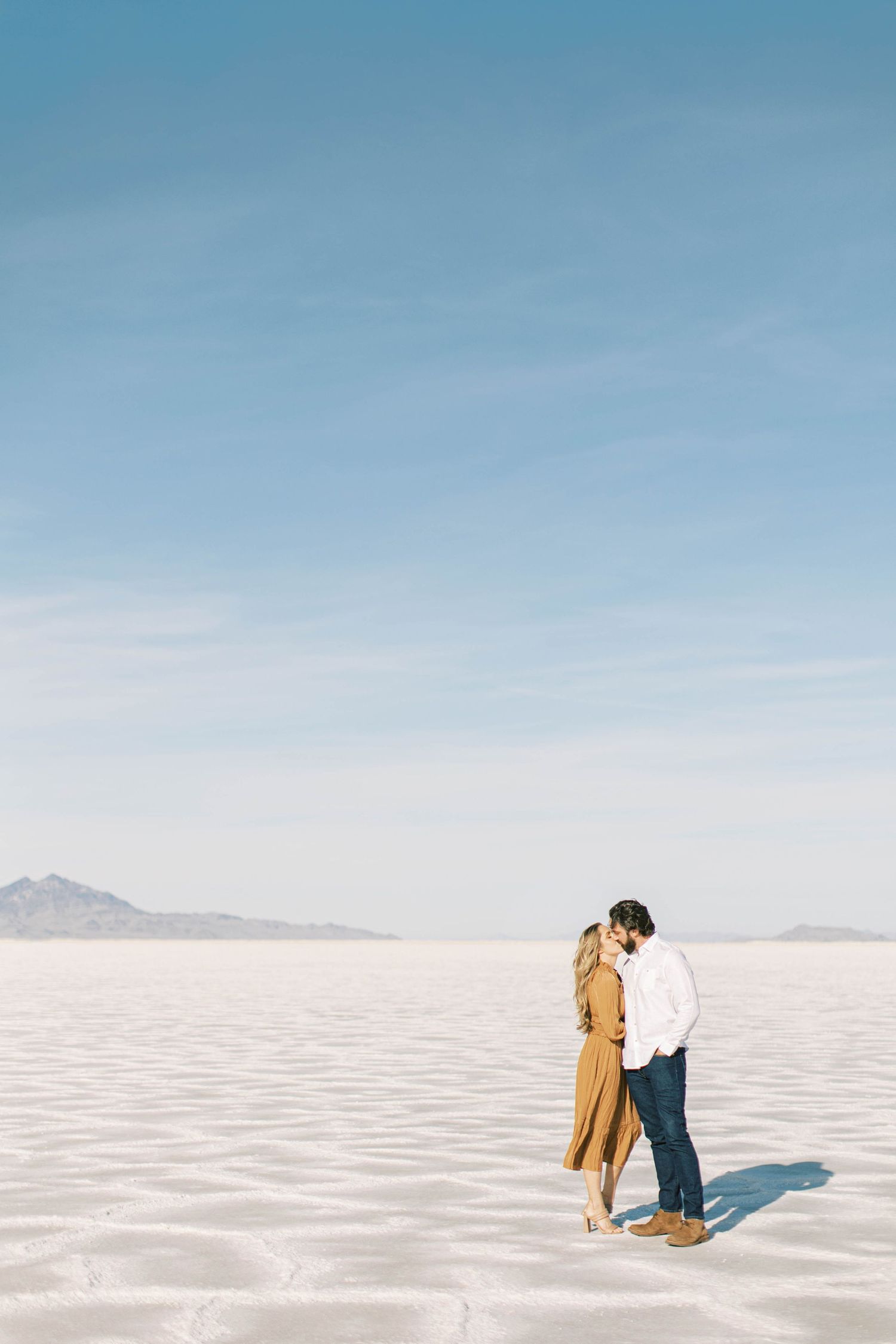 A couple stands together on the Bonneville Salt Flats against a bright blue sky.