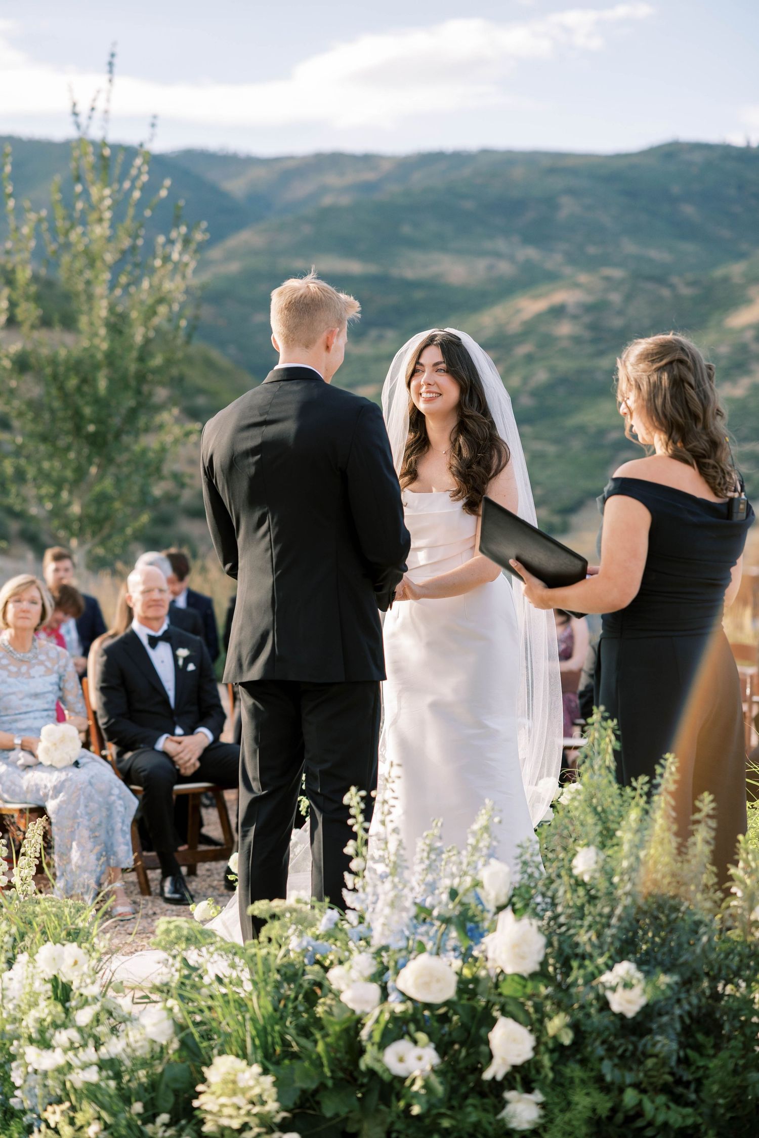 Wedding guests seated at outdoor ceremony with mountain views and white garden flowers.
