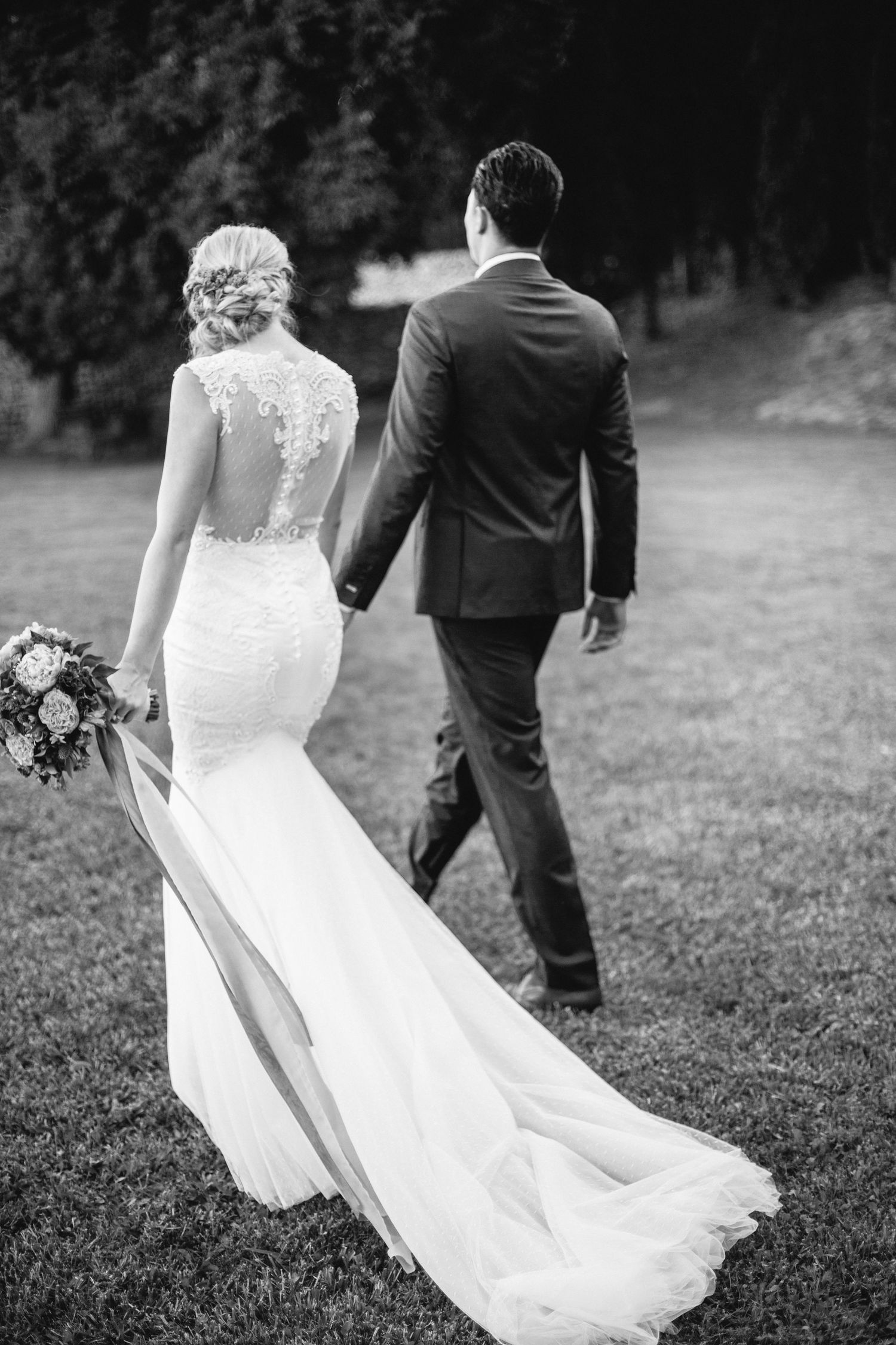 Wedding couple walking on grass showcasing bride's elegant lace back gown at chateau de moissac.