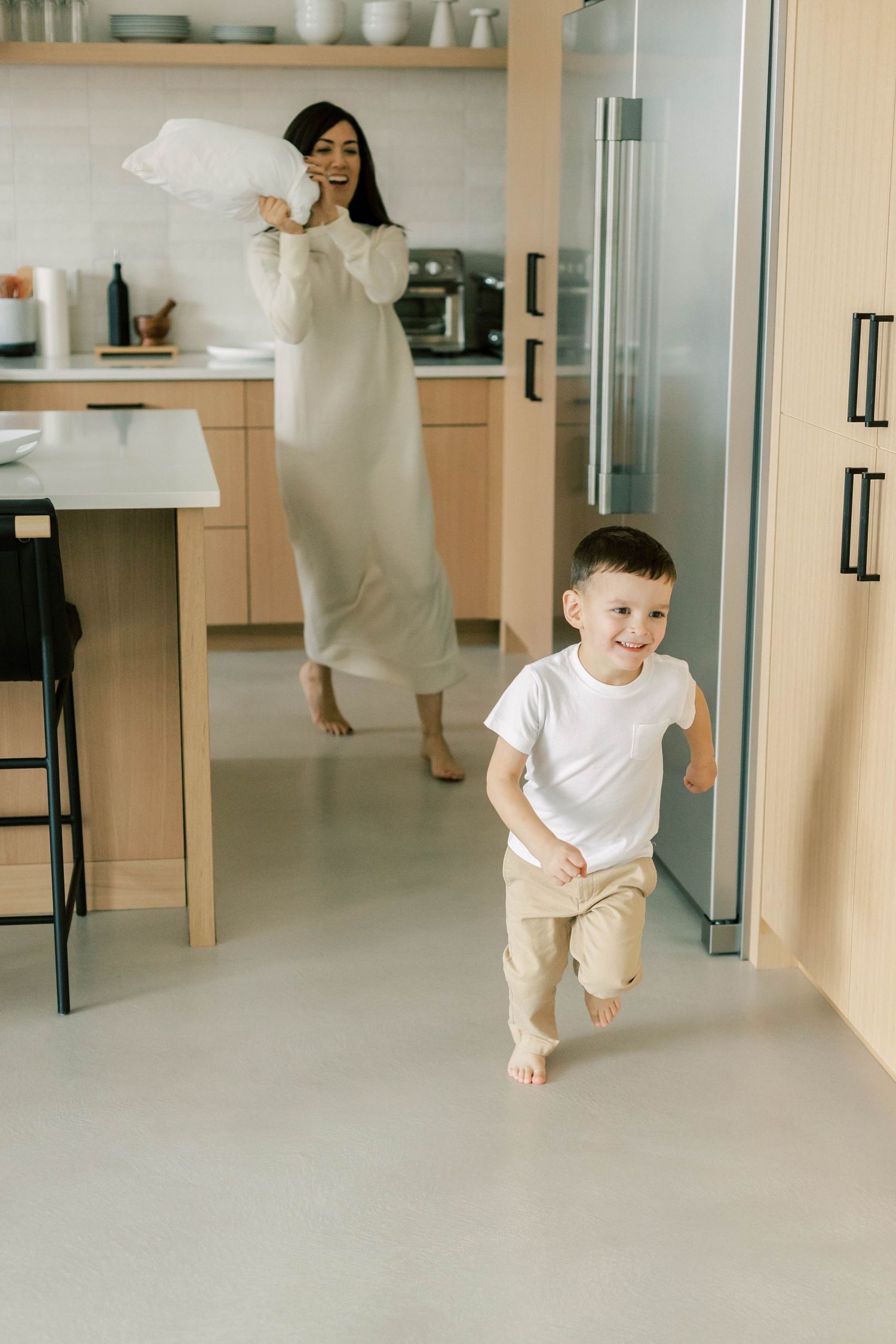 Mother and child playing chase in modern minimalist kitchen.