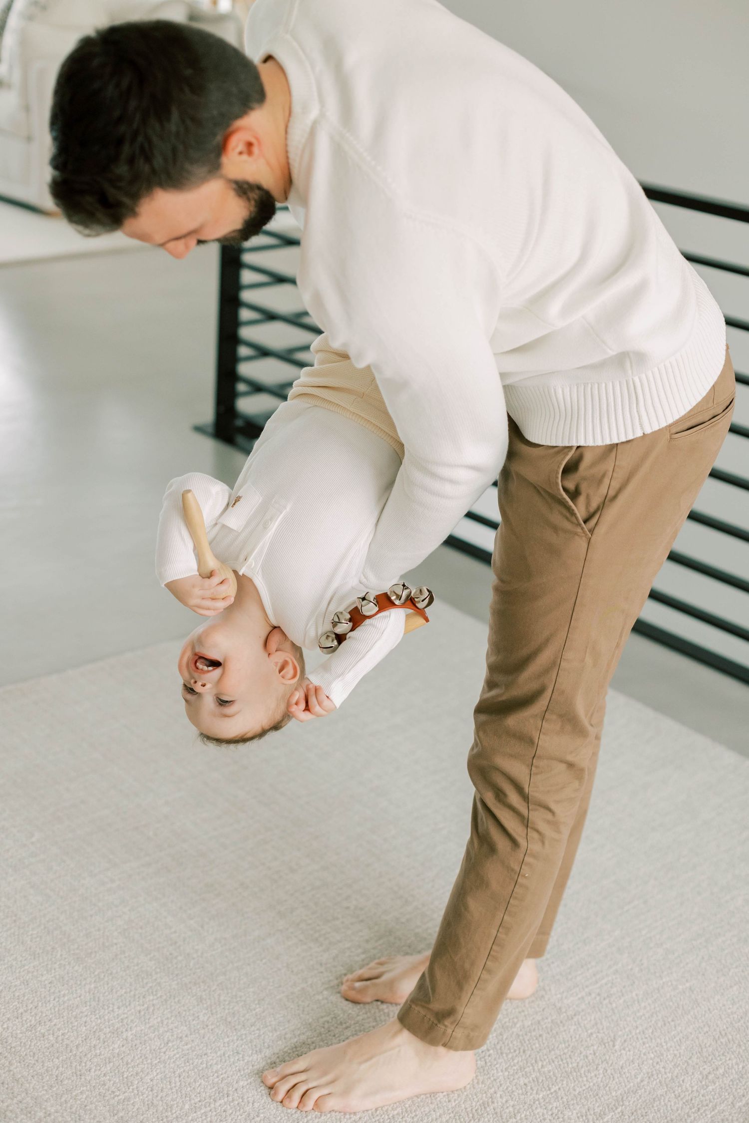 Playful parent holds laughing child upside down in modern home setting.