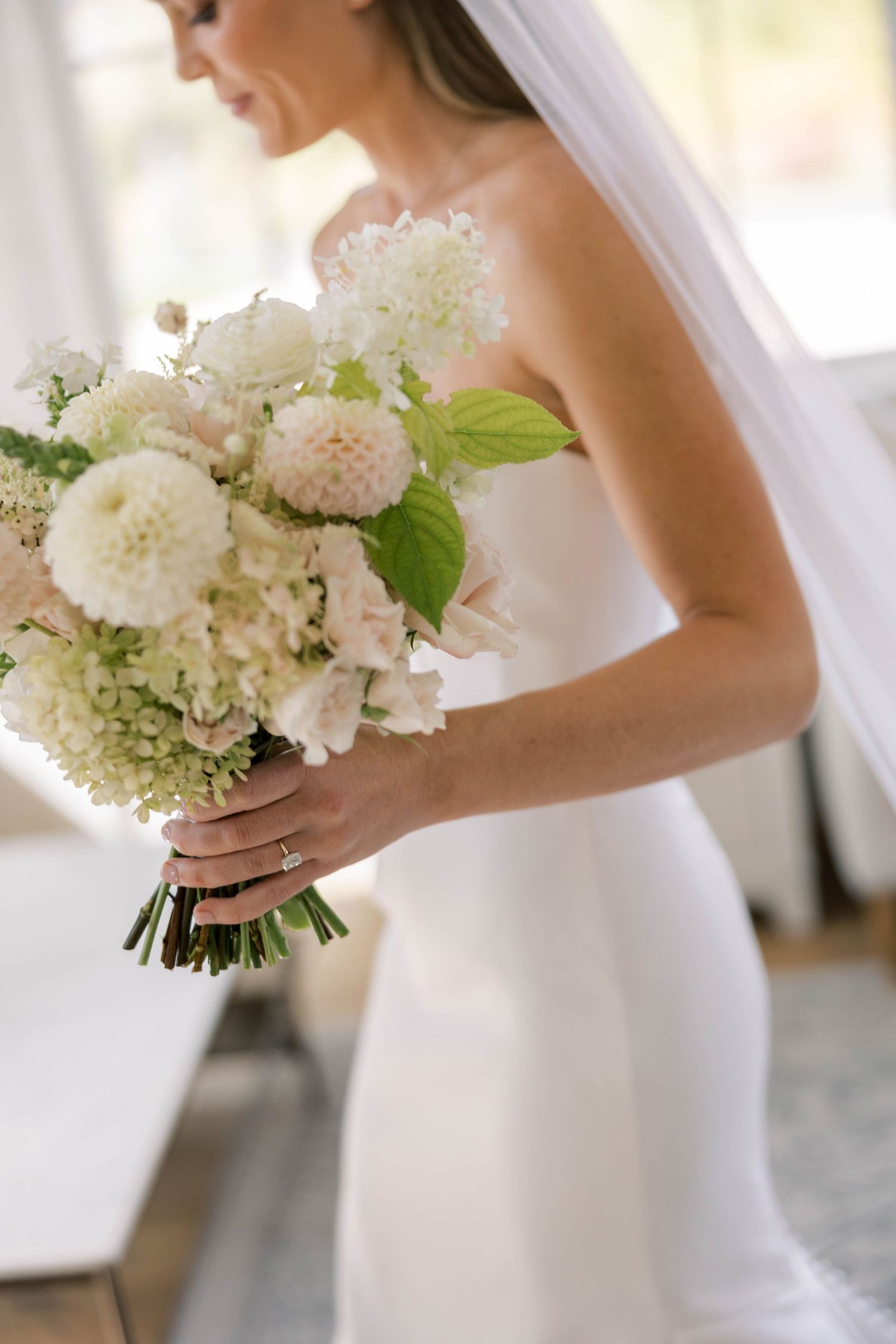 An elegant bridal bouquet features white dahlias, roses and delicate greenery against a simple white dress.