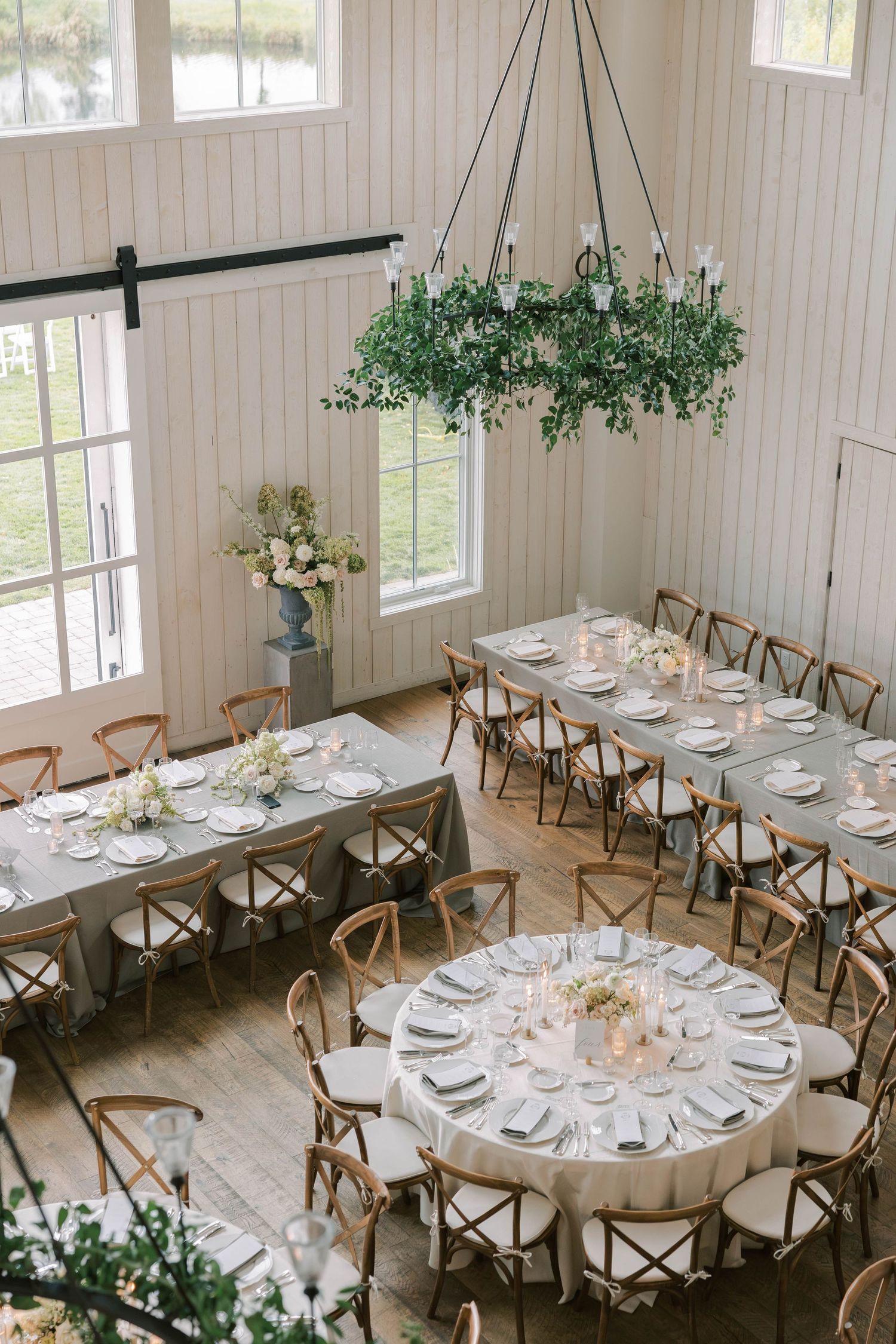 Elegant wedding reception venue with round tables, cross-back chairs, and white shiplap walls in a bright airy space.