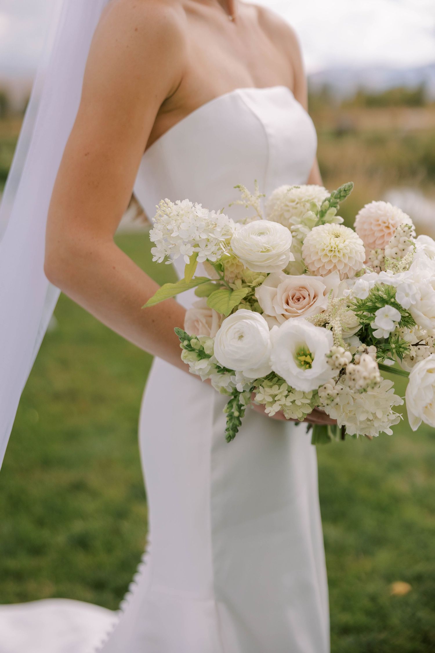 Close-up details of an elegant white and blush wedding bouquet with roses and dahlias.