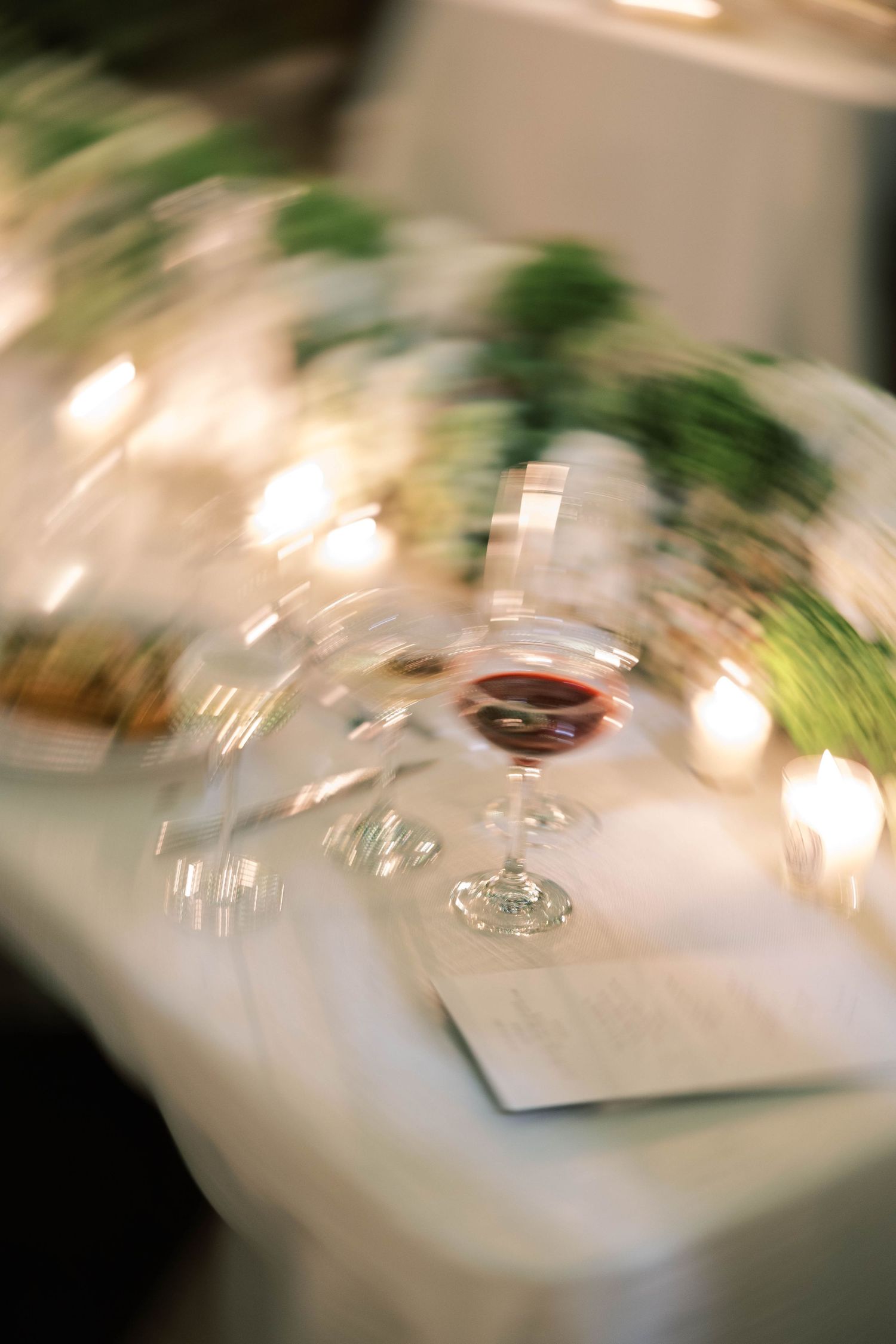 Artistic blurred photo of elegant table setting with wine glass and greenery decorations in soft focus.