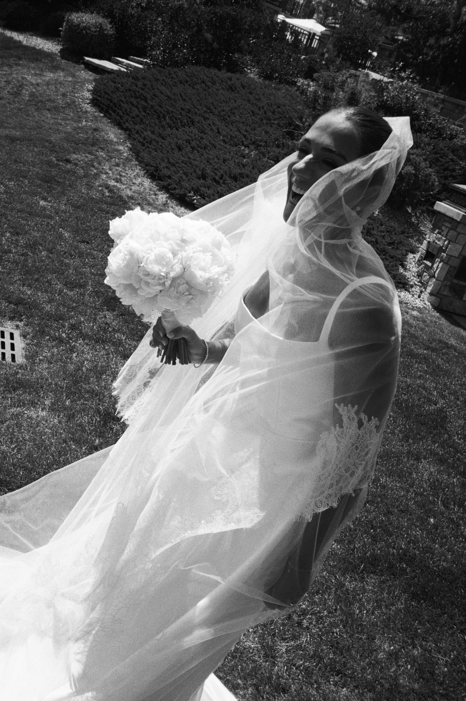 A flowing white wedding veil billows dramatically in the wind against a dark grassy background.