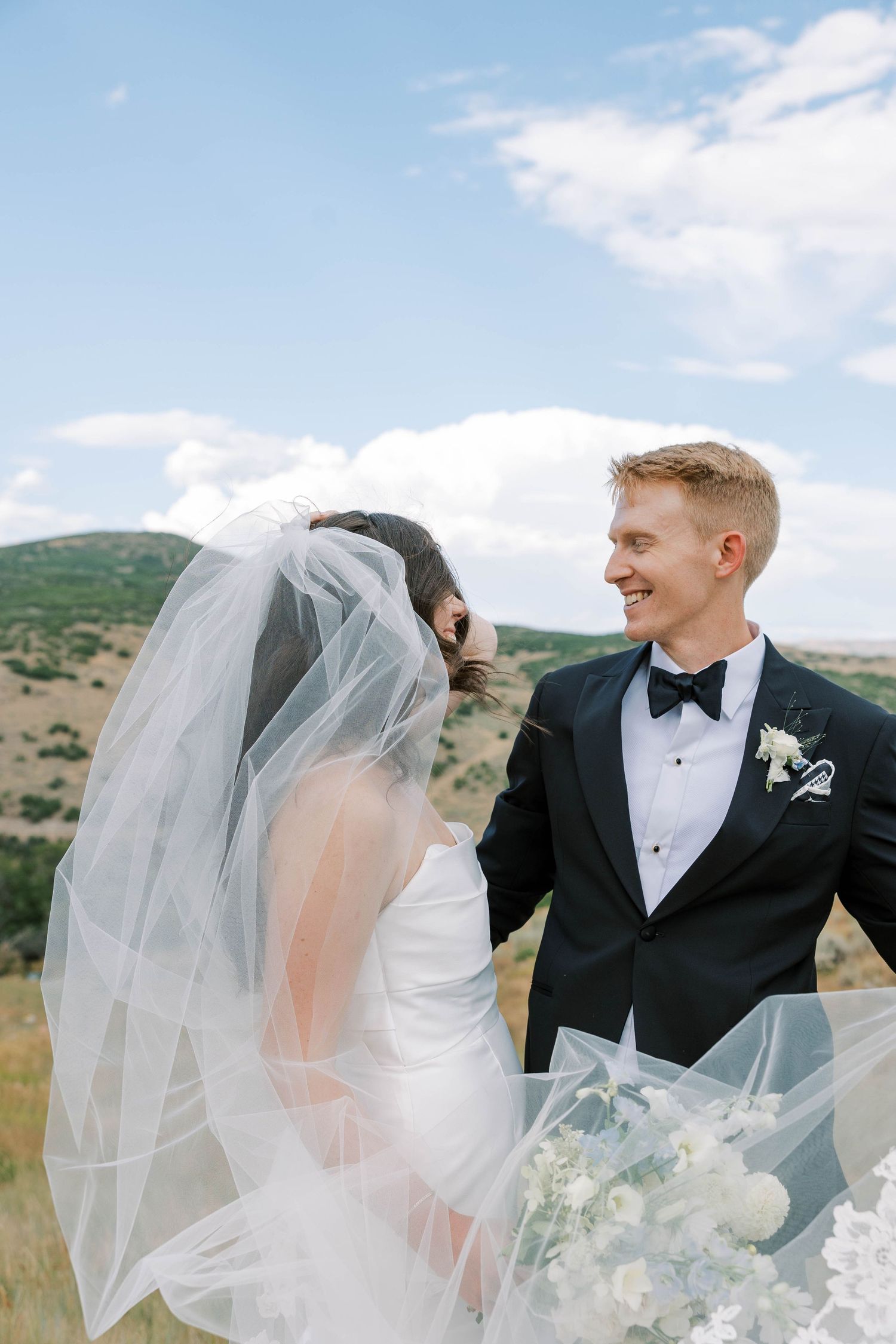Candid wedding moments captured against rolling hills and blue sky backdrop.