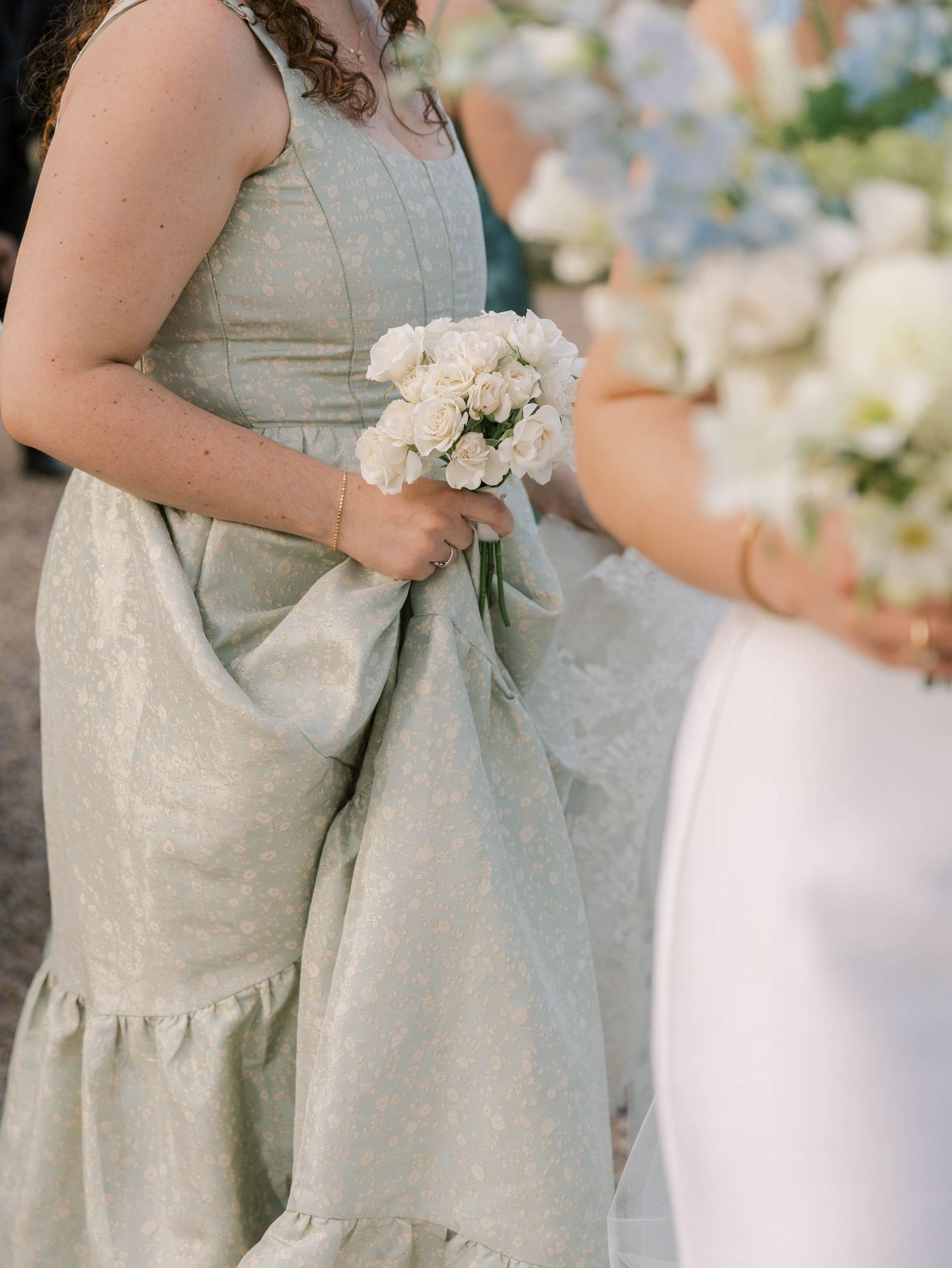 Row of bridesmaids in soft gray dresses holding white bouquets at an elegant wedding.