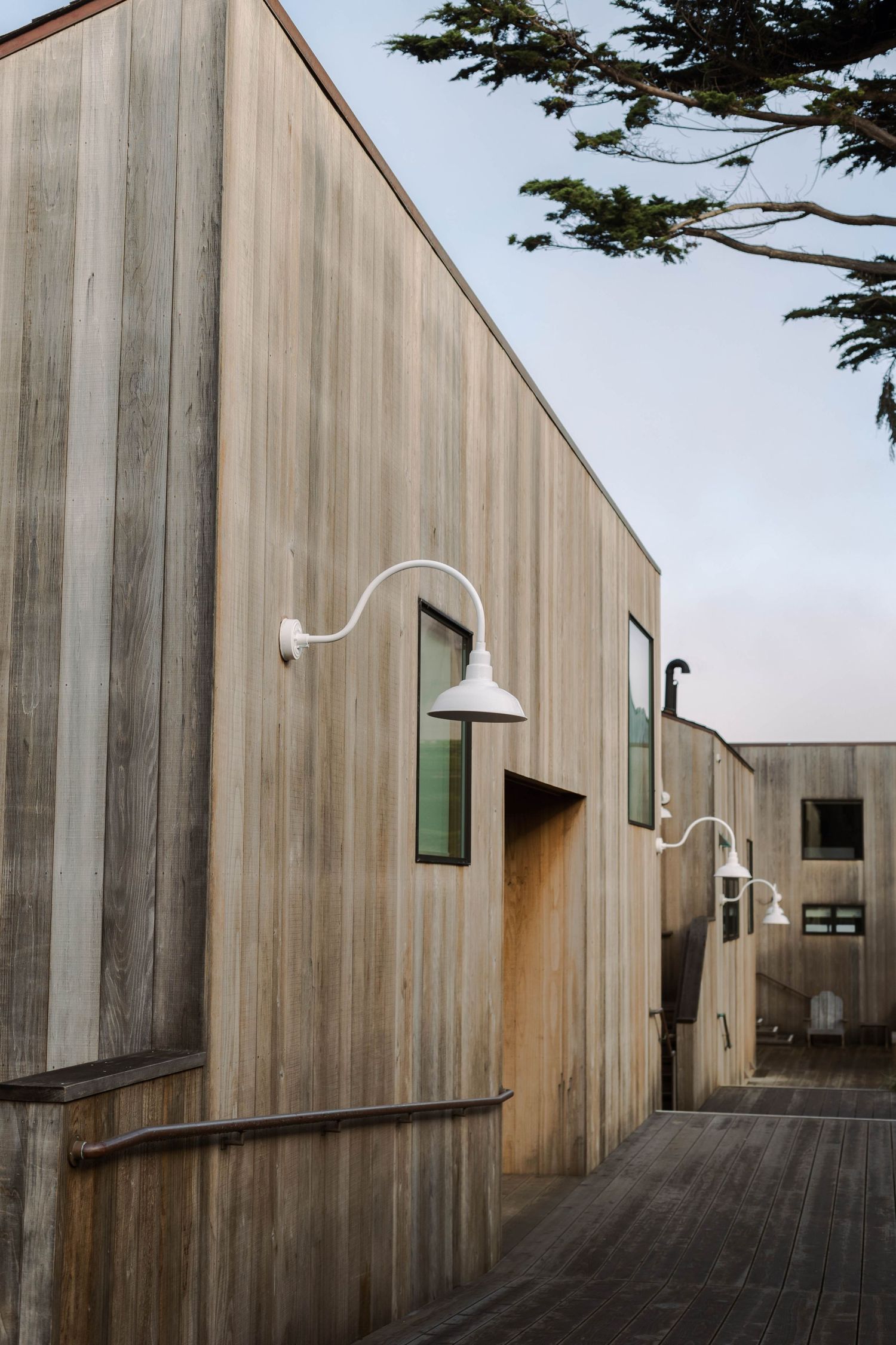 Modern wooden building exterior with curved walls and deck features weathered gray siding and minimalist design elements.
