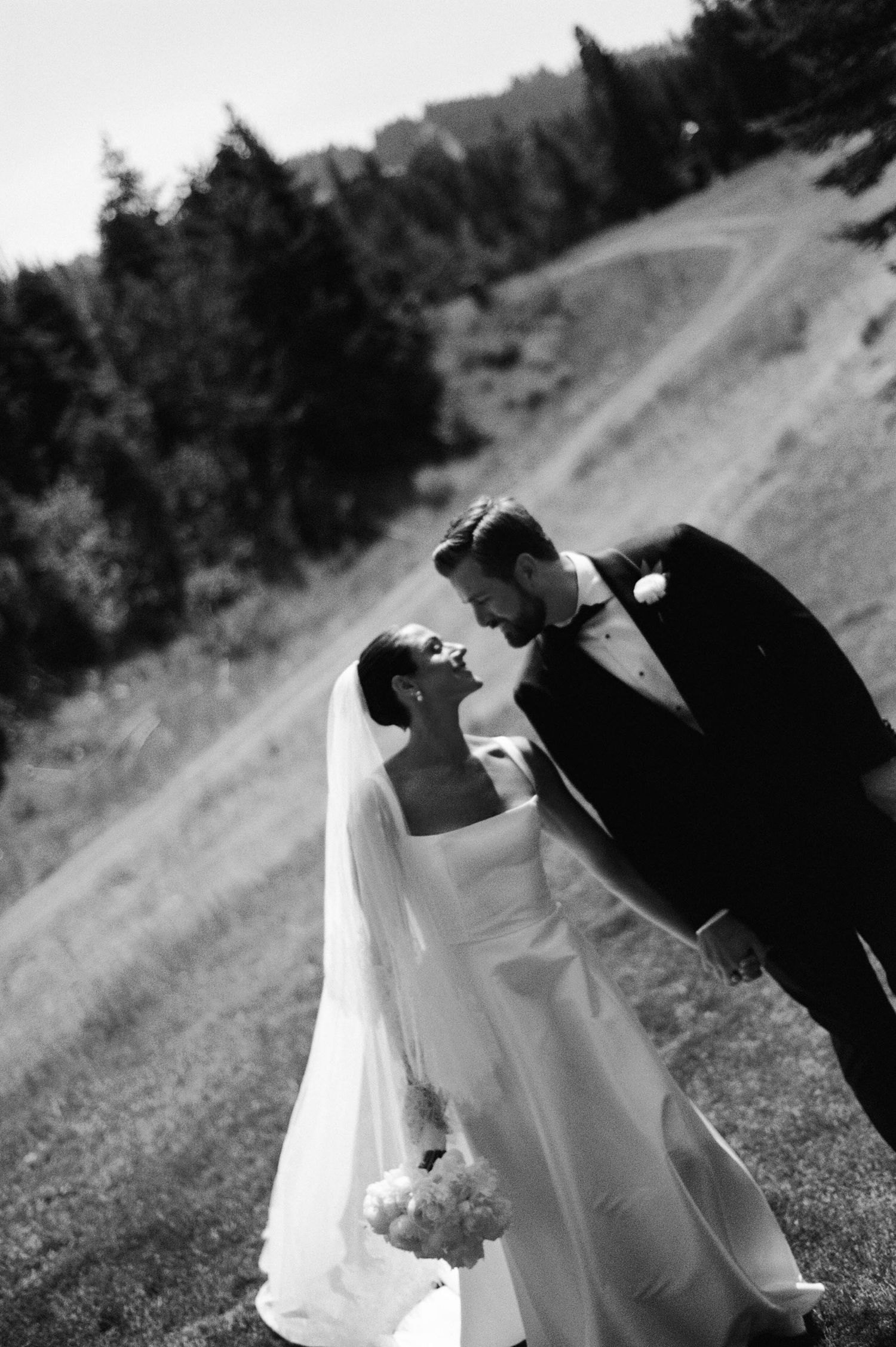 Black and white wedding photo series showing a romantic dip kiss between newlyweds on a grassy hillside.
