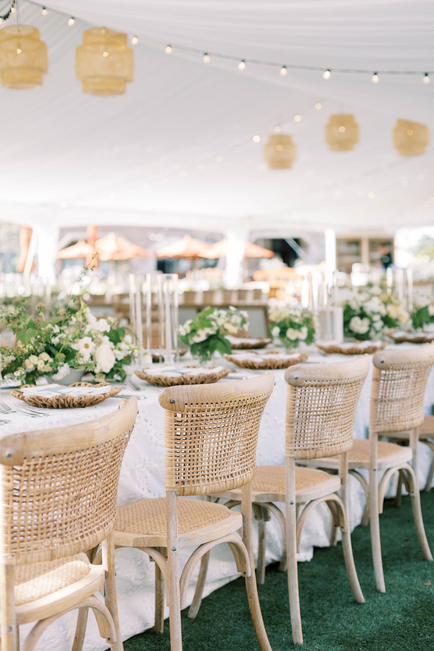Row of rattan dining chairs under hanging lanterns in a white tent wedding reception at everline resort lake tahoe.
