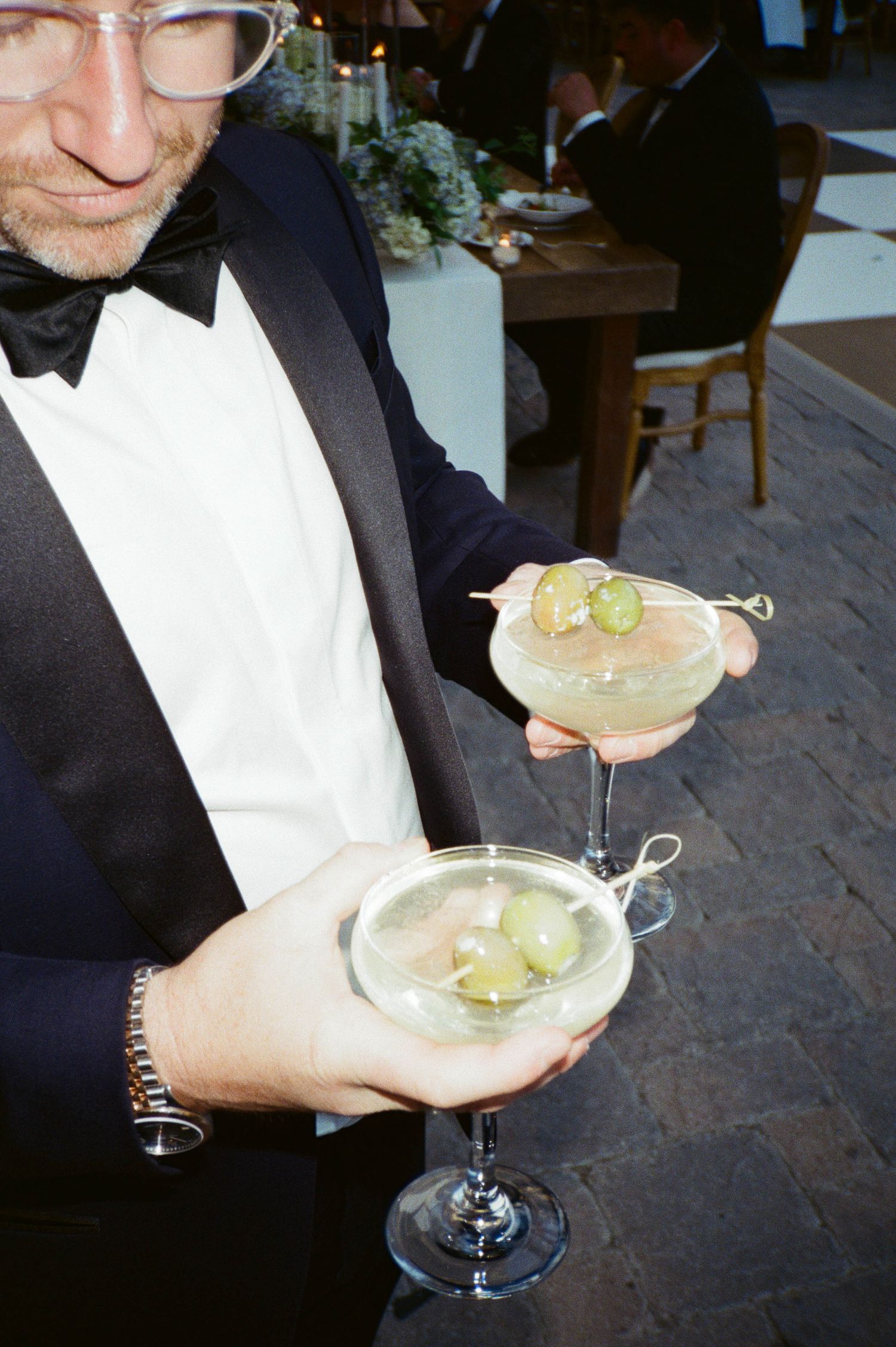 Four elegant cocktail glasses garnished with grapes and filled with a light-colored beverage are held at a formal event.