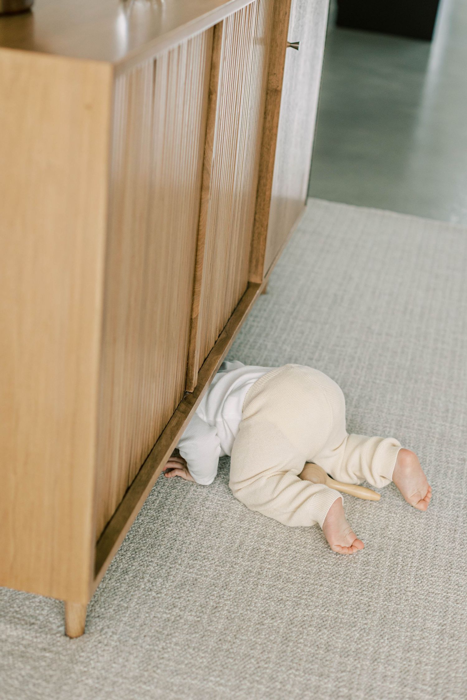Small child crawling on gray carpet behind wooden furniture.