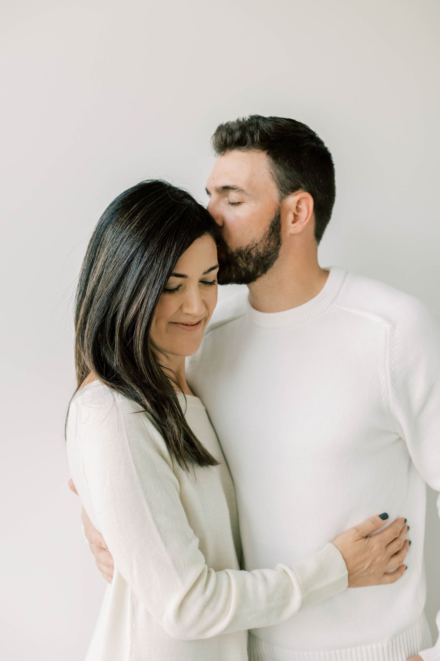 Couple in white embracing tenderly against minimal white background.