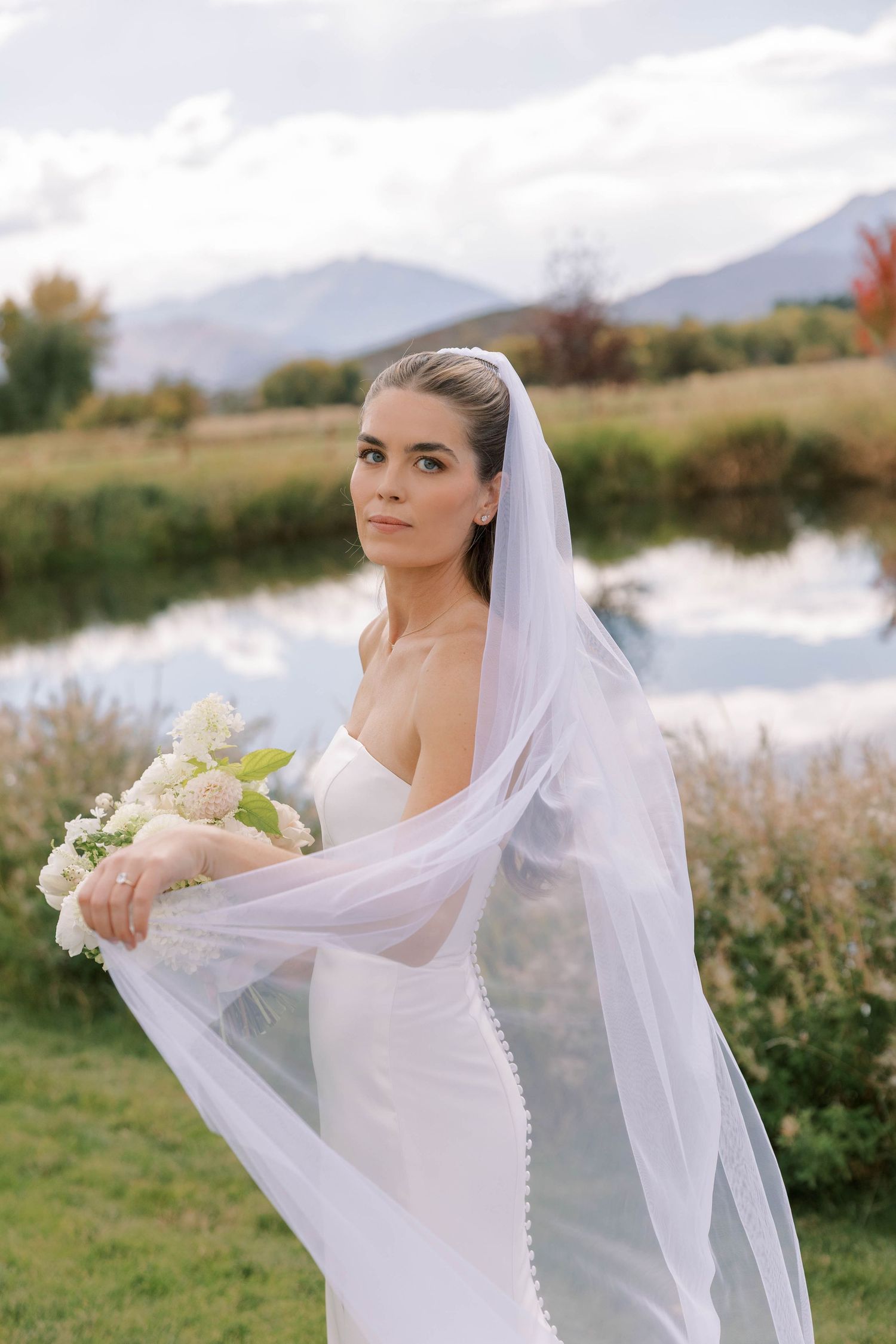 Scenic lakeside wedding portrait with mountains and autumn foliage in background.