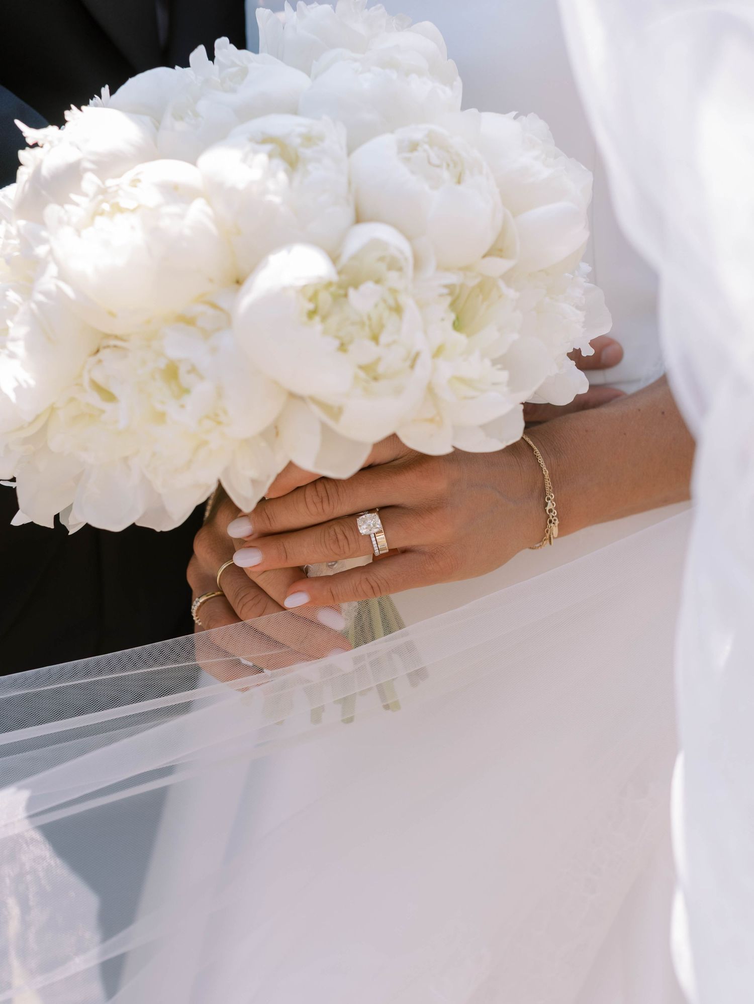Close-up view of white peony bridal bouquet with diamond engagement ring detail.