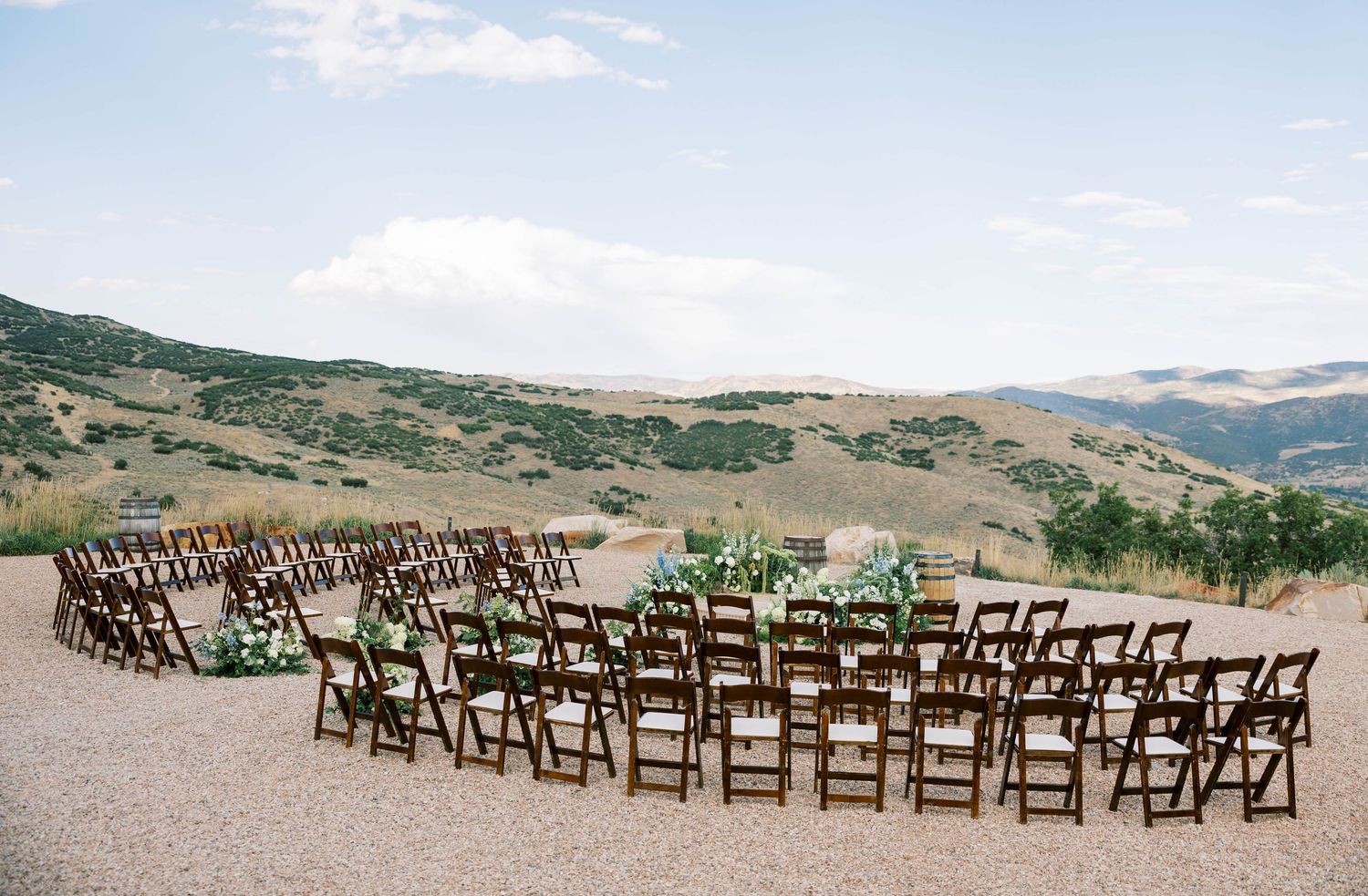 Wooden ceremony chairs arranged in curved rows on a scenic hillside overlooking mountains and valleys.