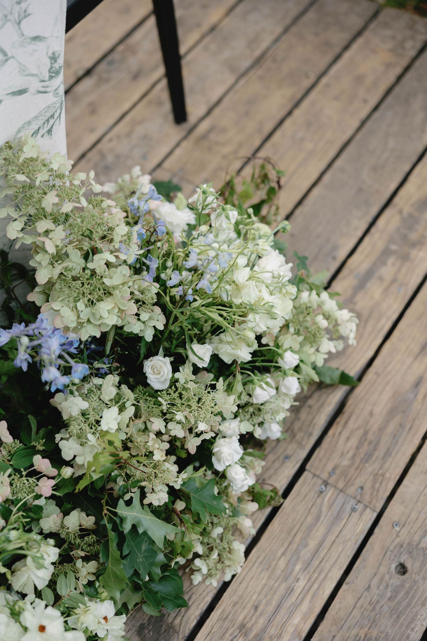White hydrangea and delicate floral arrangement displayed on rustic wooden deck planks.