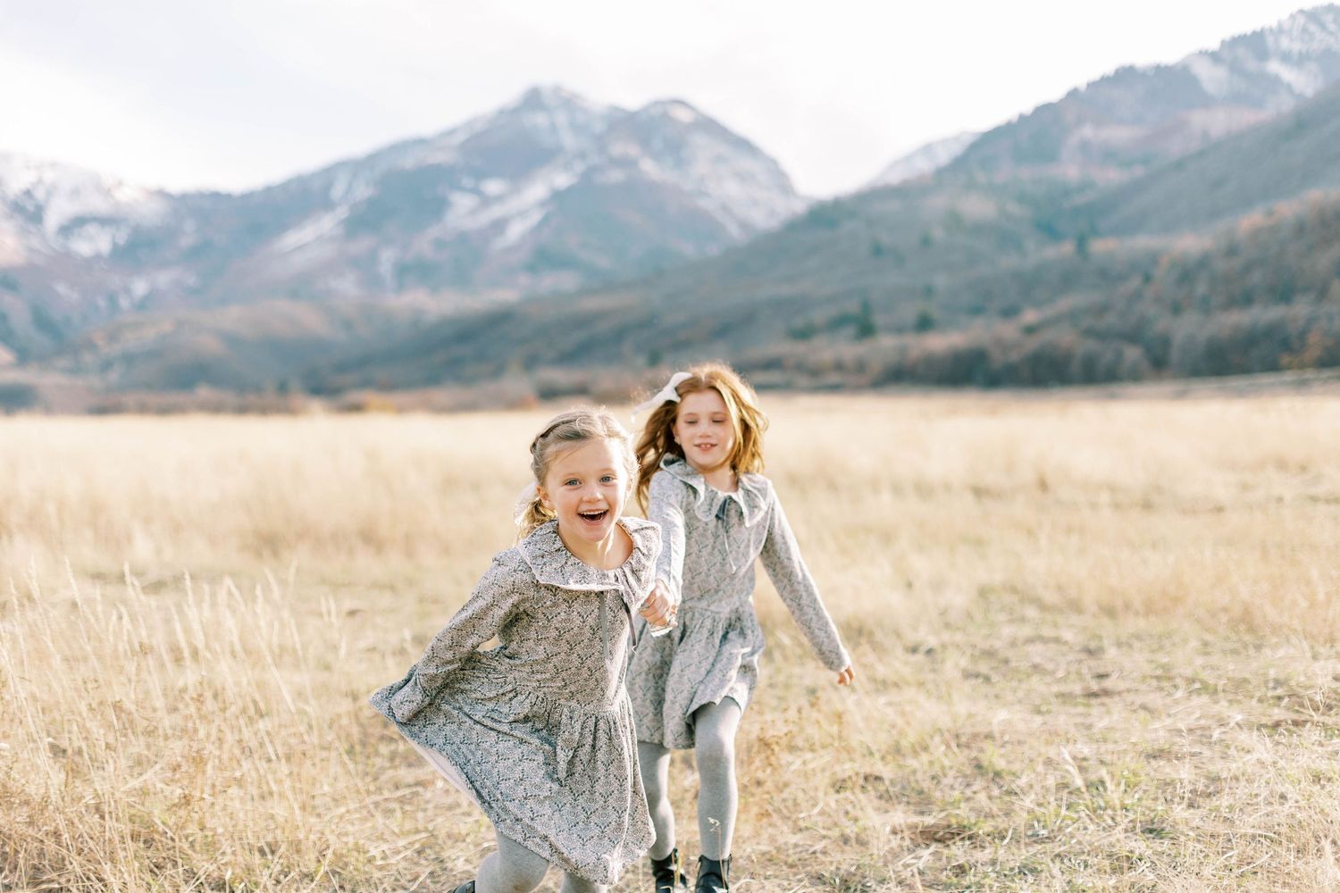 Children running joyfully through tall grass with mountains in background.