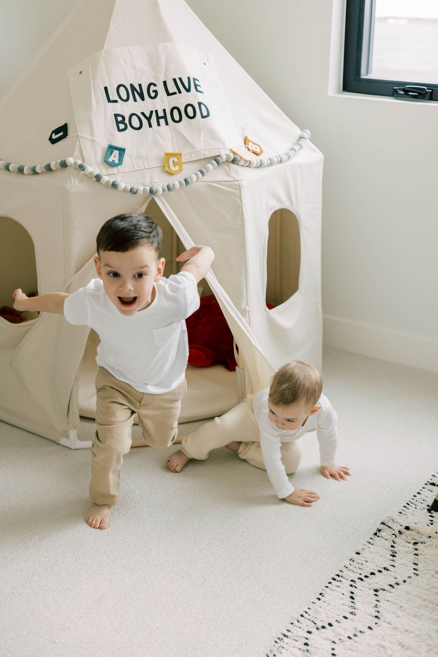 Two children playing in white teepee tent with 'Long Live Boyhood' text.