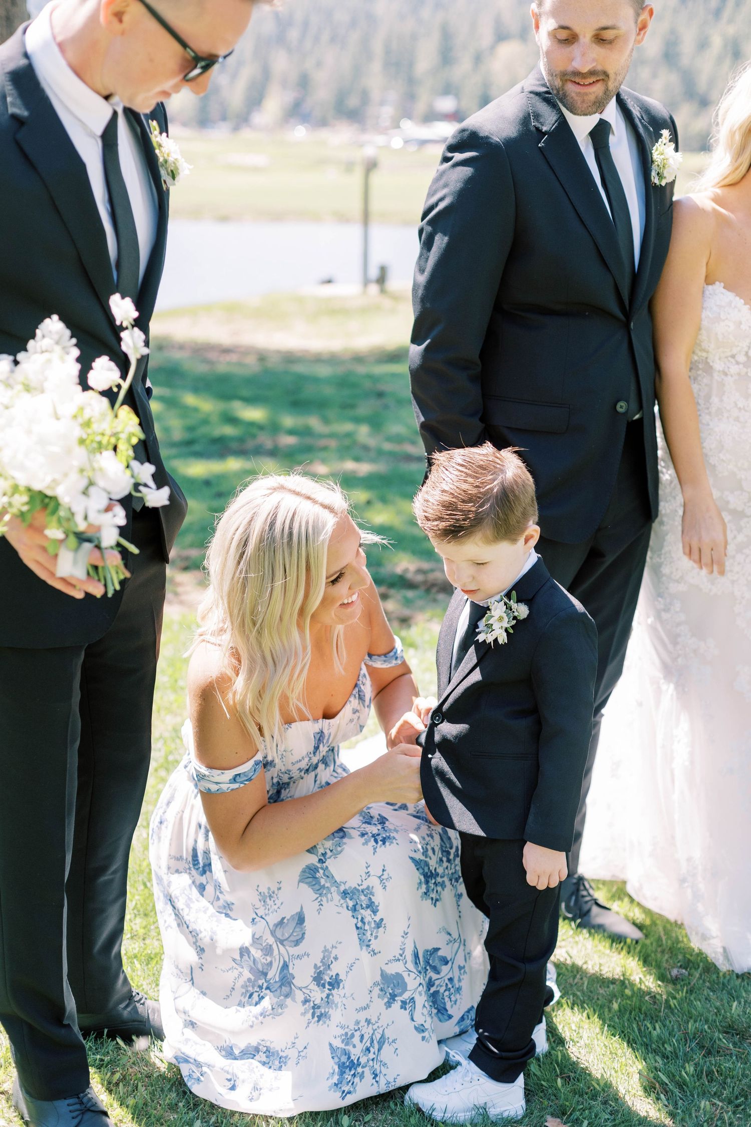 Wedding party members gather on a grassy lawn during an outdoor ceremony.