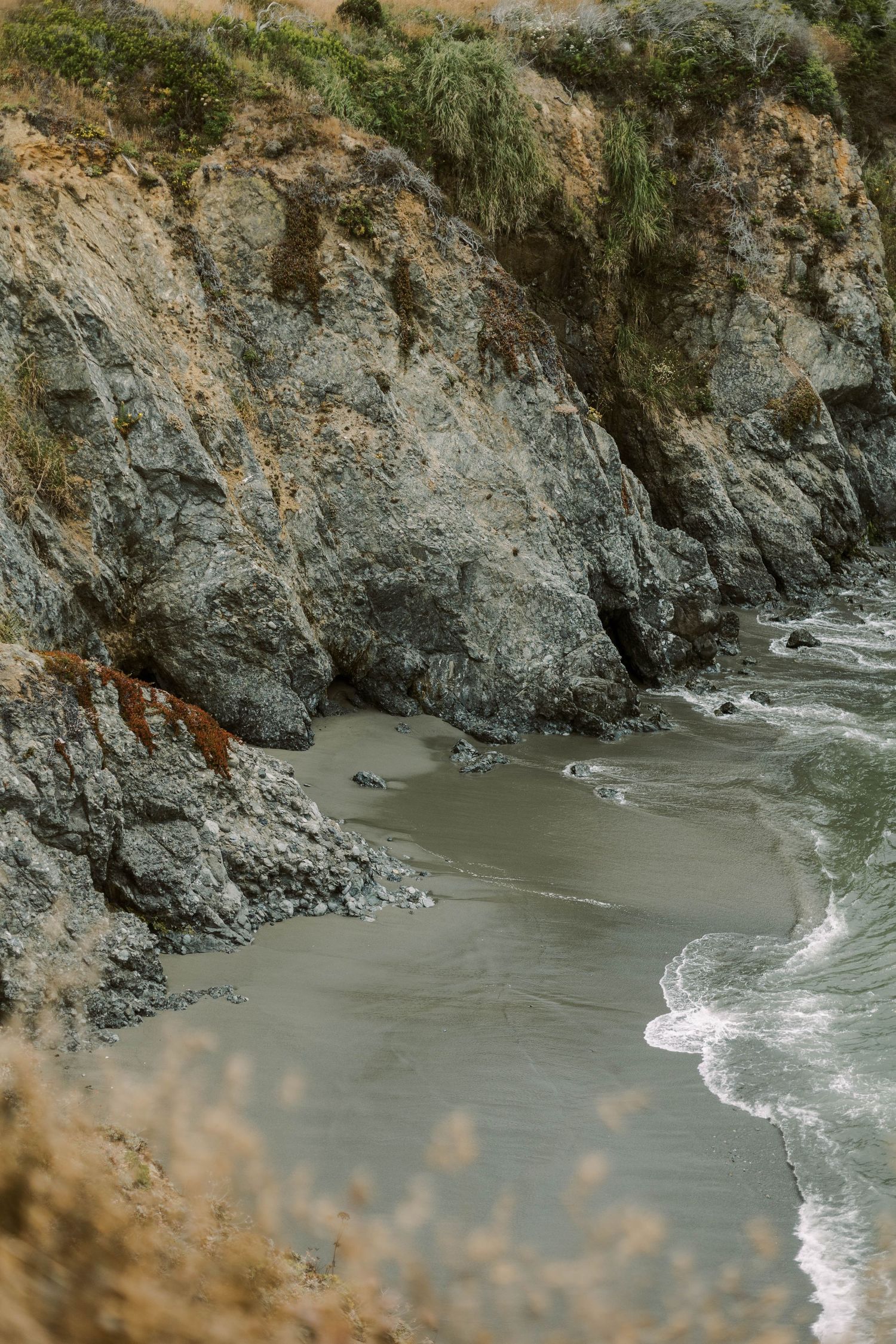 Rocky coastal cliffs meet the ocean waves along a secluded beach cove with dramatic geological formations.