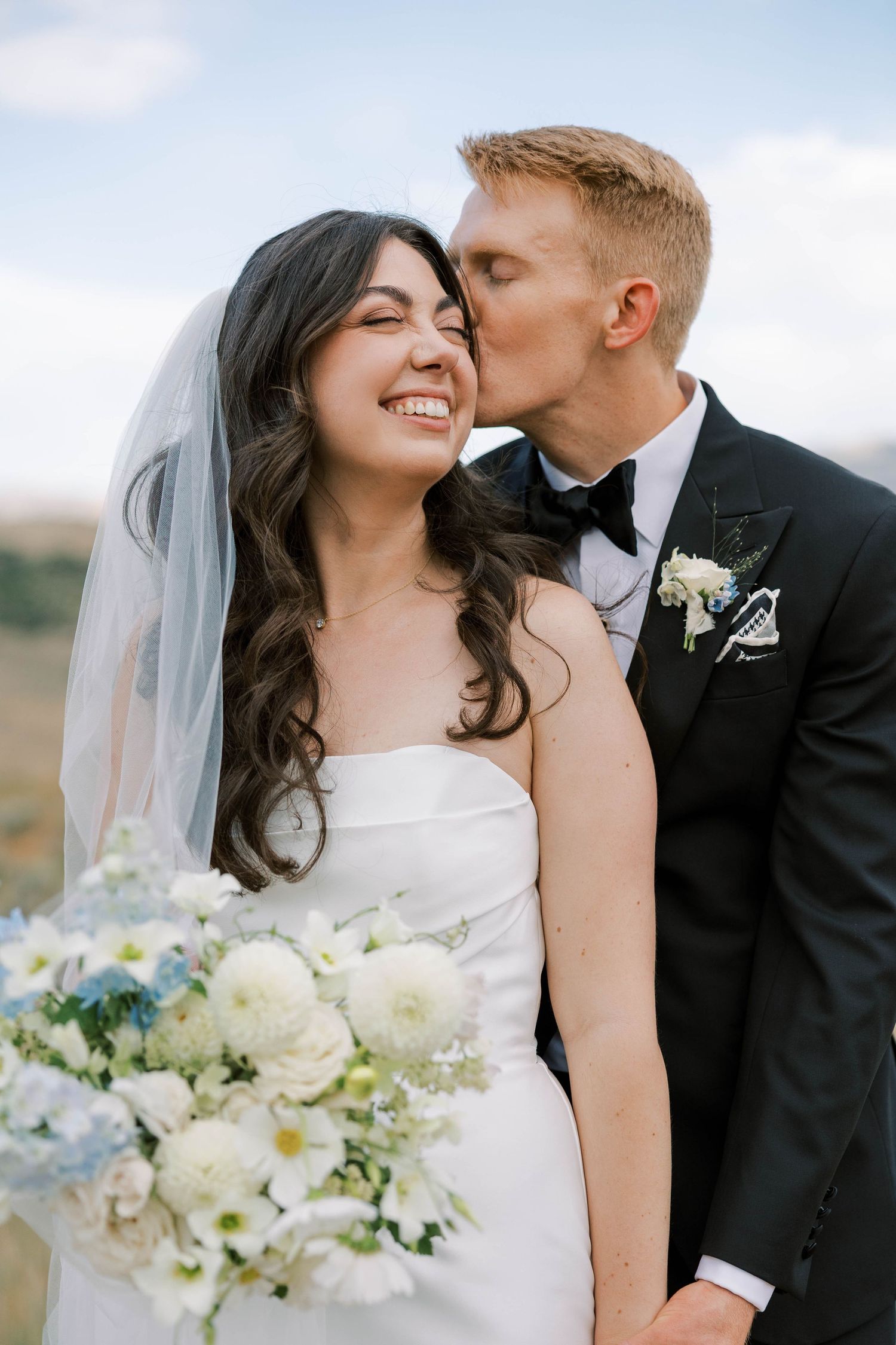 A joyful wedding moment captured outdoors with a beautiful bouquet of white flowers against a natural landscape.