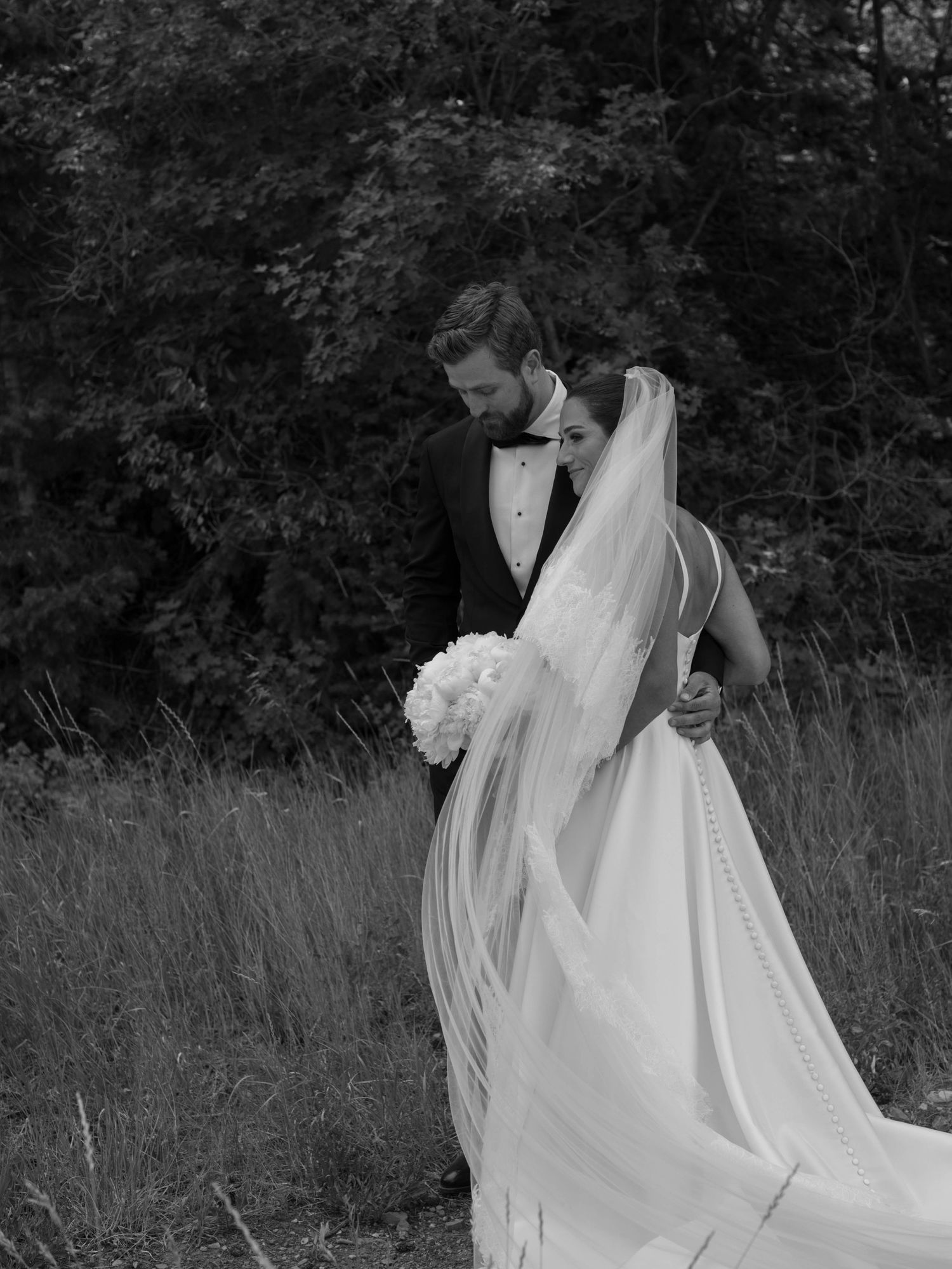 Black and white photo of a flowing white wedding dress moving gracefully in a meadow setting.
