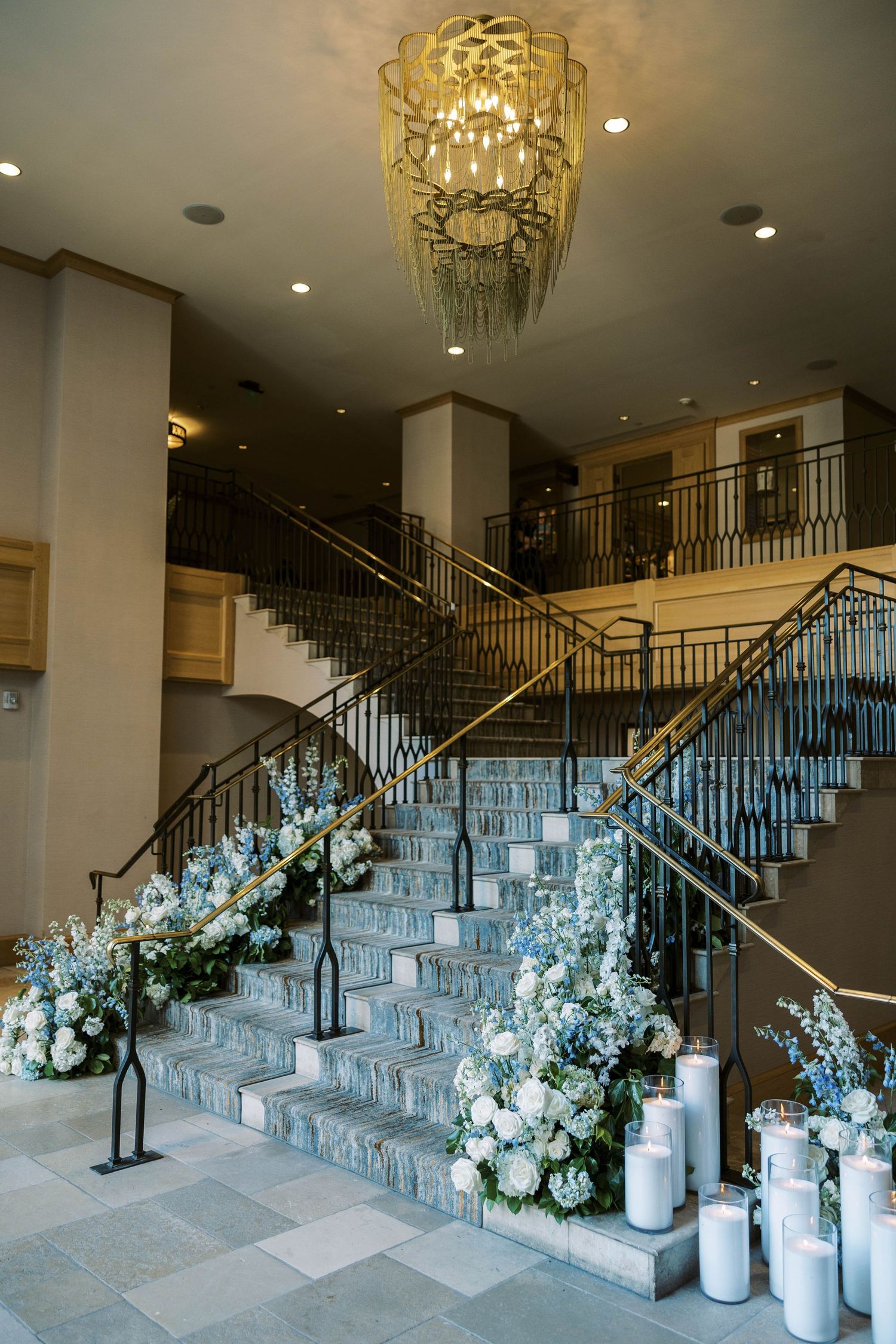 Elegant staircase decorated with white floral arrangements and candles in a grand ballroom entrance.