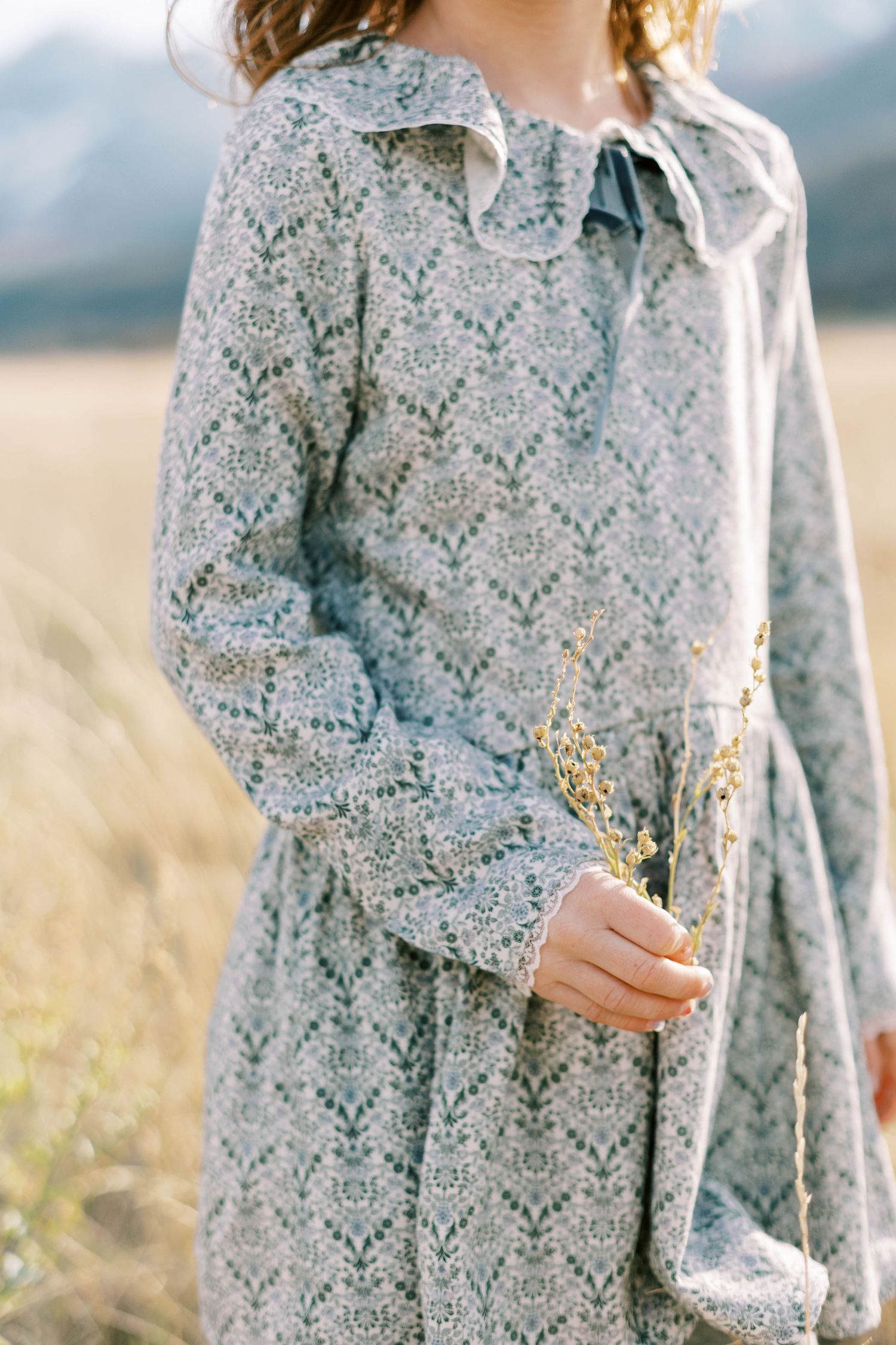 Close-up details of vintage-style gray floral dress with delicate pattern in outdoor setting.