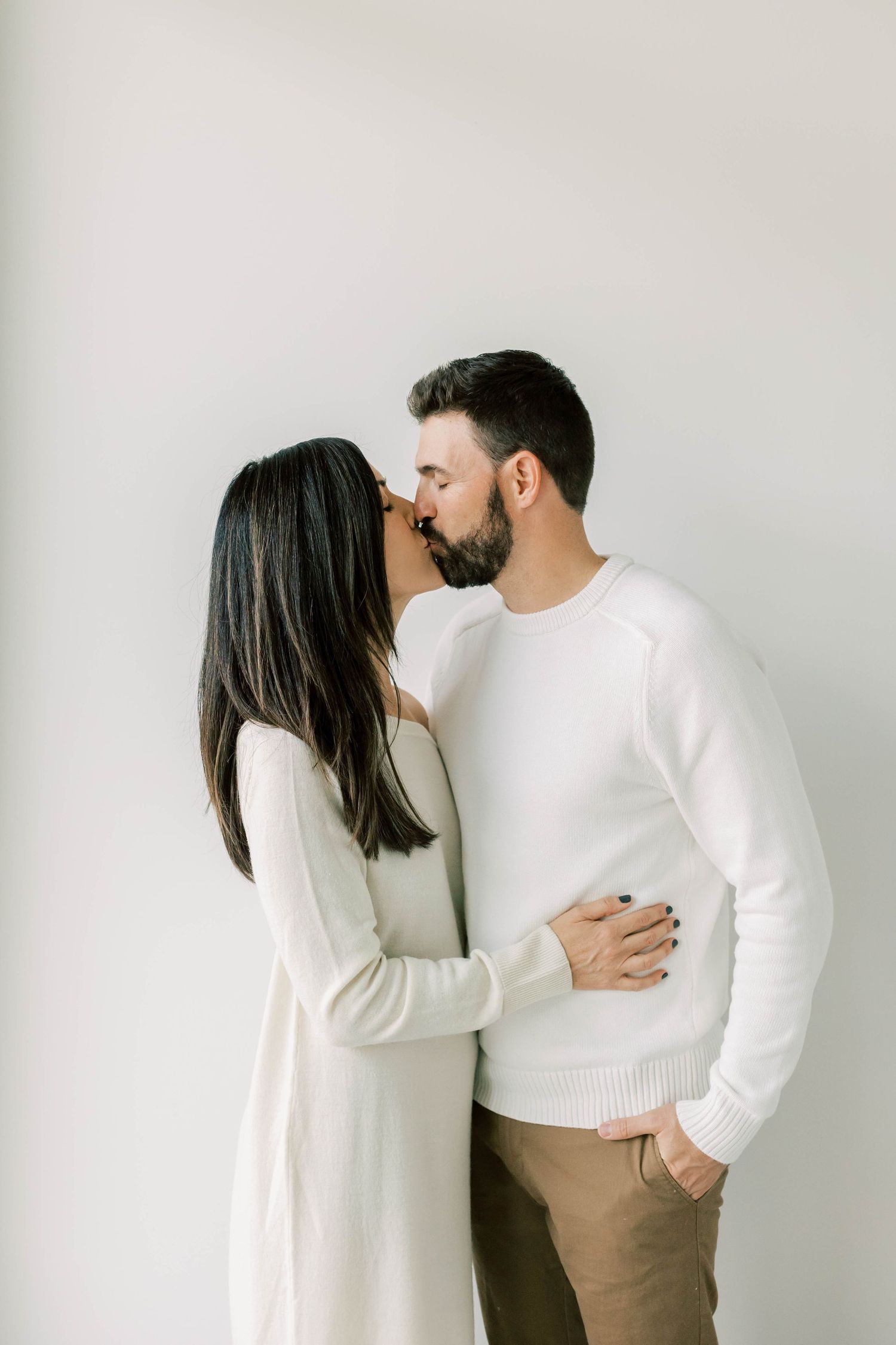 Intimate couple in white sweaters sharing romantic moment against white wall.