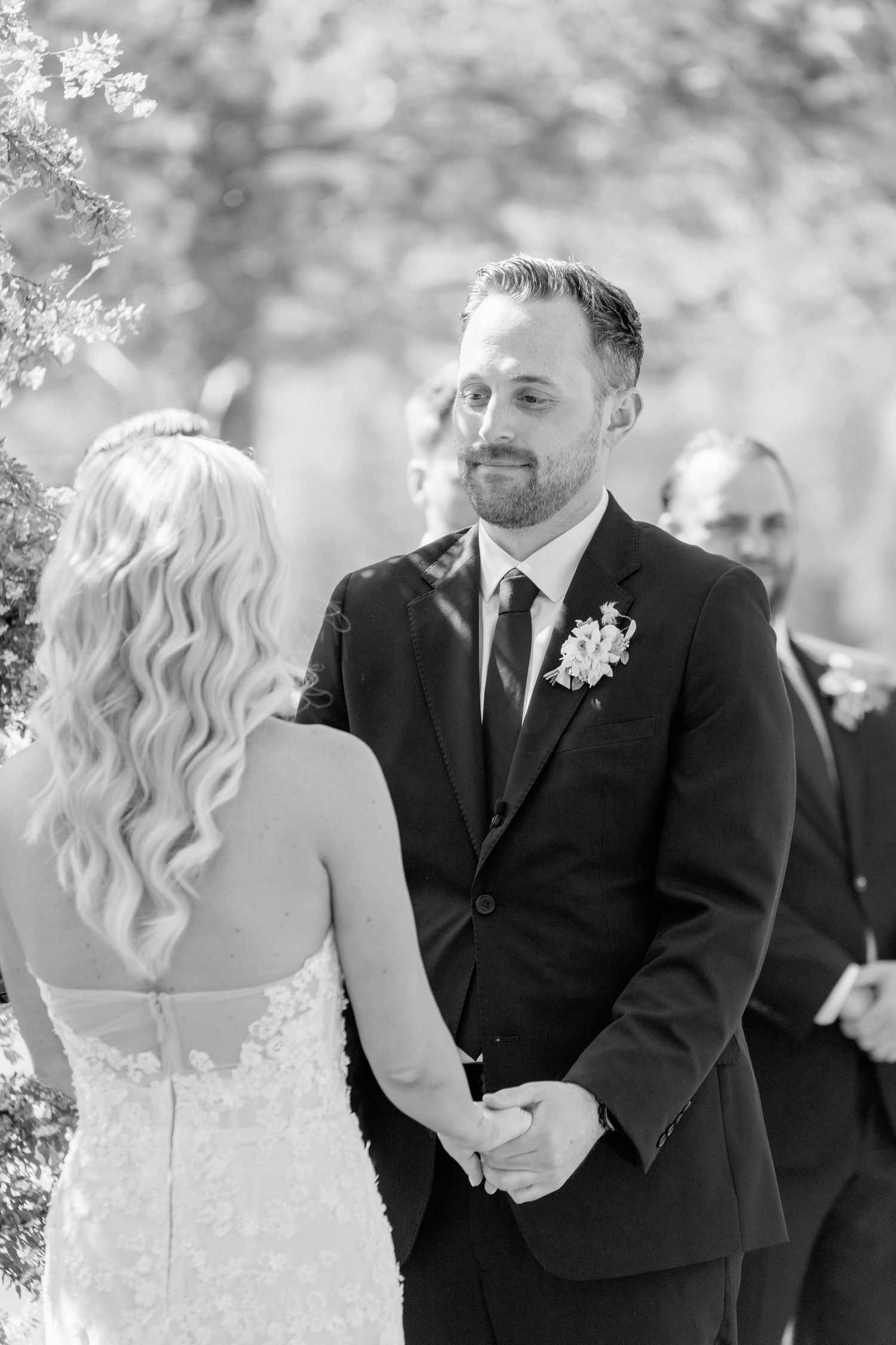 Wedding ceremony moment in black and white with couple holding hands under blooming trees.