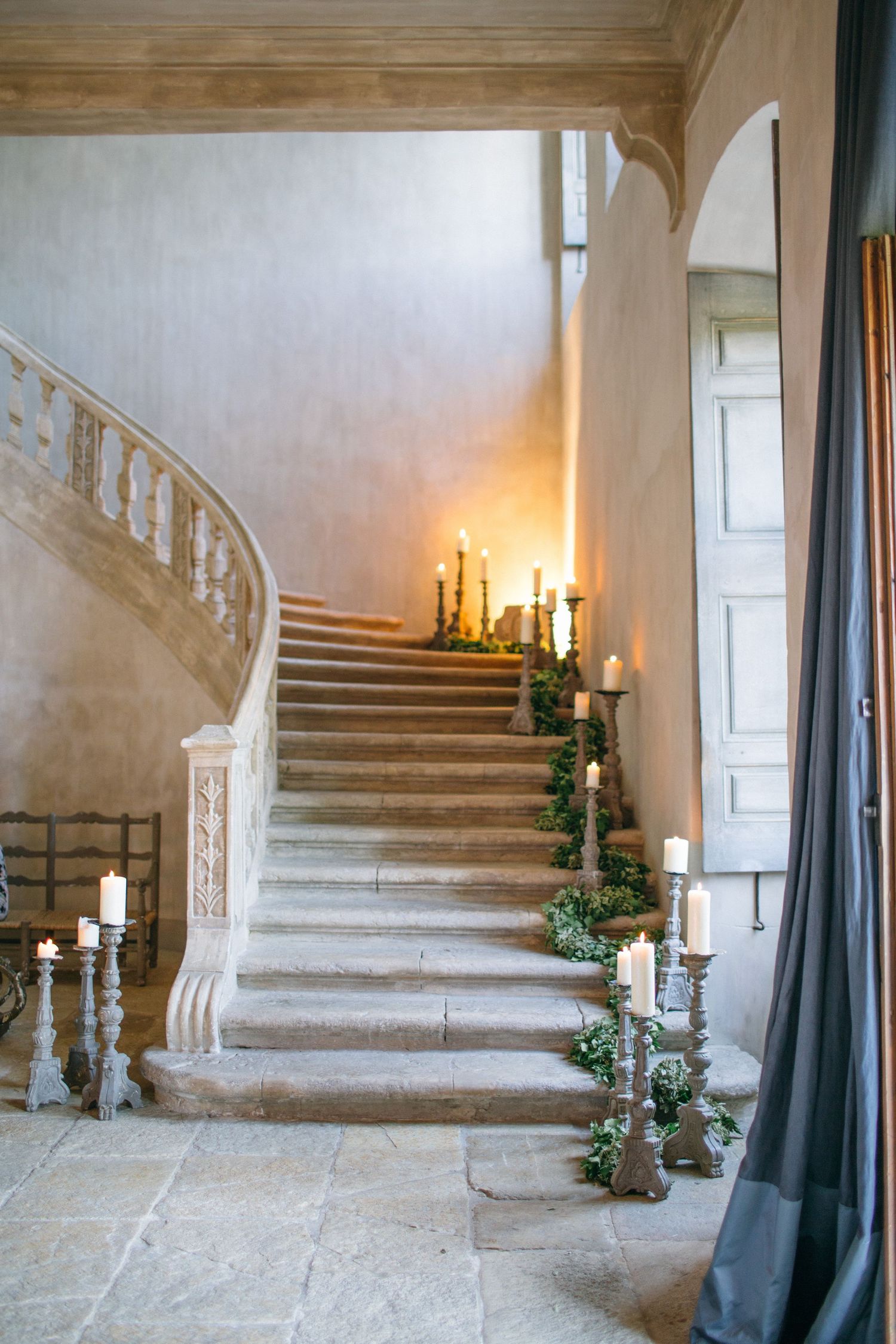 Elegant curved staircase decorated with greenery and glowing candles in stone castle interior at chateau de moissac.