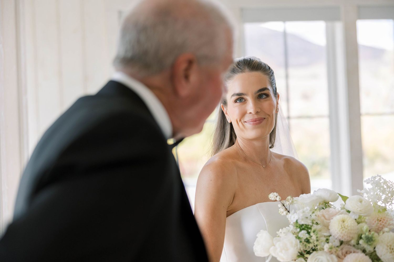 A joyful wedding scene with white floral bouquets and elegant formal attire in a bright indoor setting.