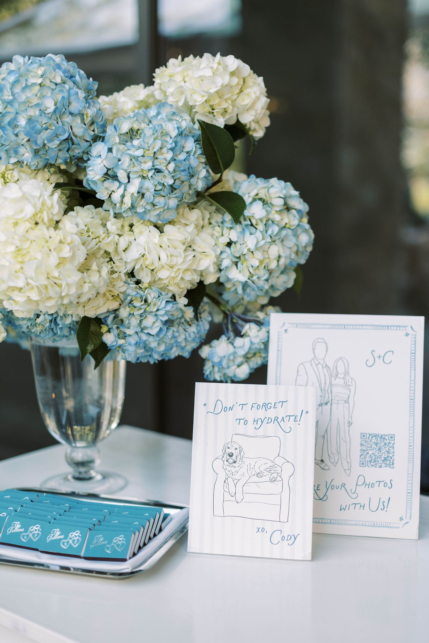 Blue and white hydrangea centerpieces with handwritten cards displayed on tables at an elegant event setting.
