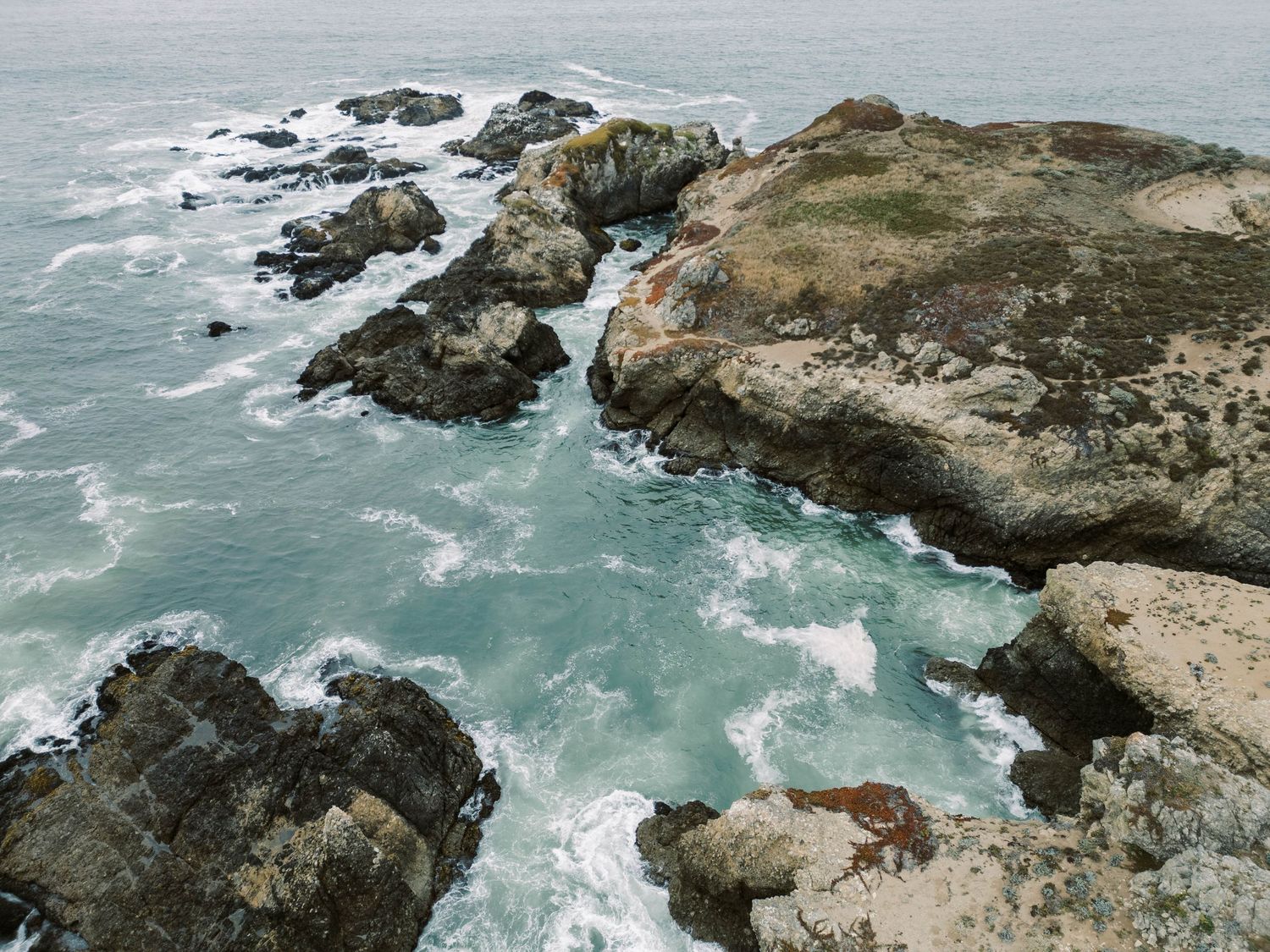 Rugged coastal cliffs meet turquoise ocean waves crashing against rocky shores along a dramatic Pacific coastline.