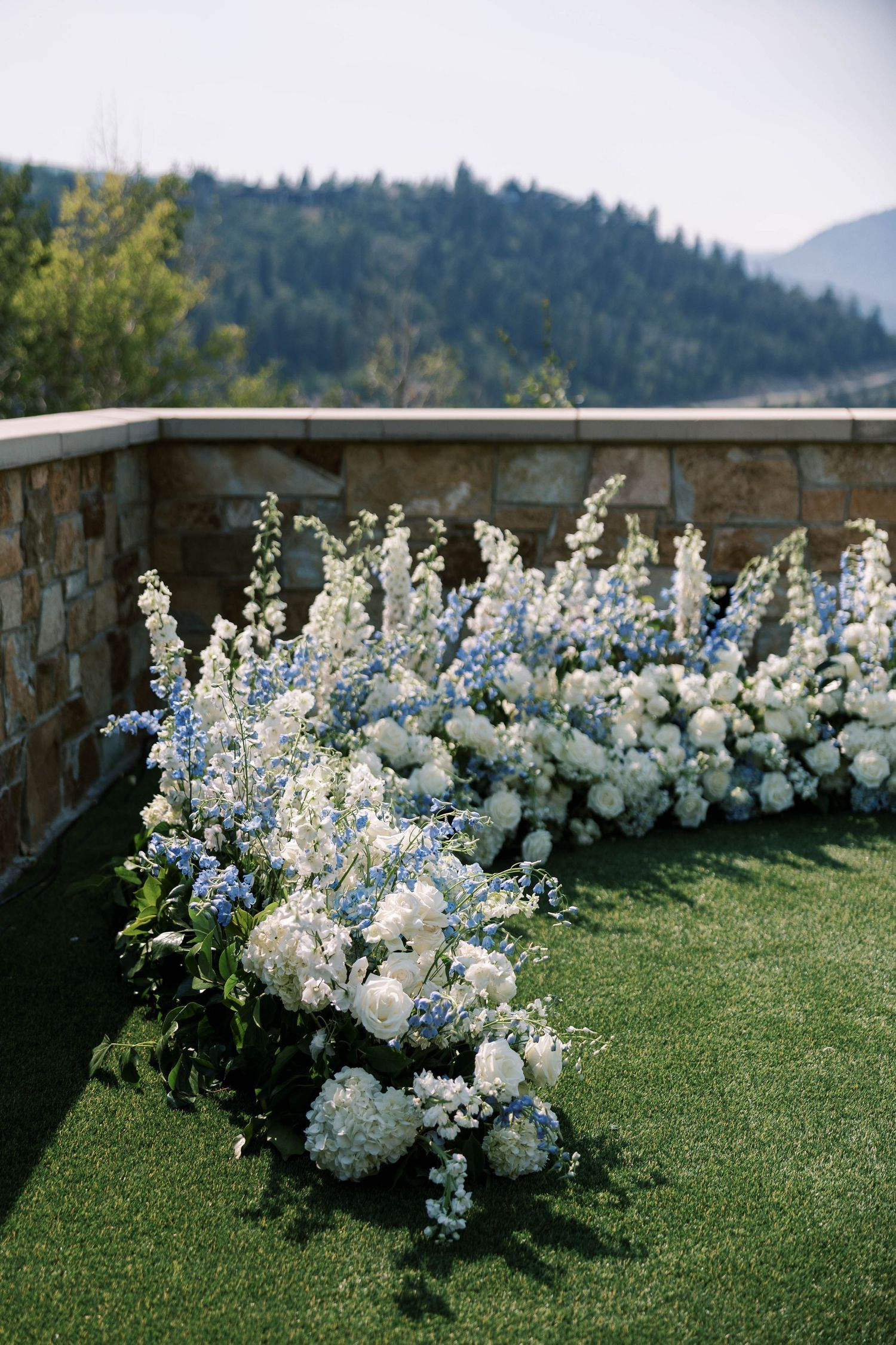 White and blue floral arrangements line a grassy outdoor venue with mountain views in the background.