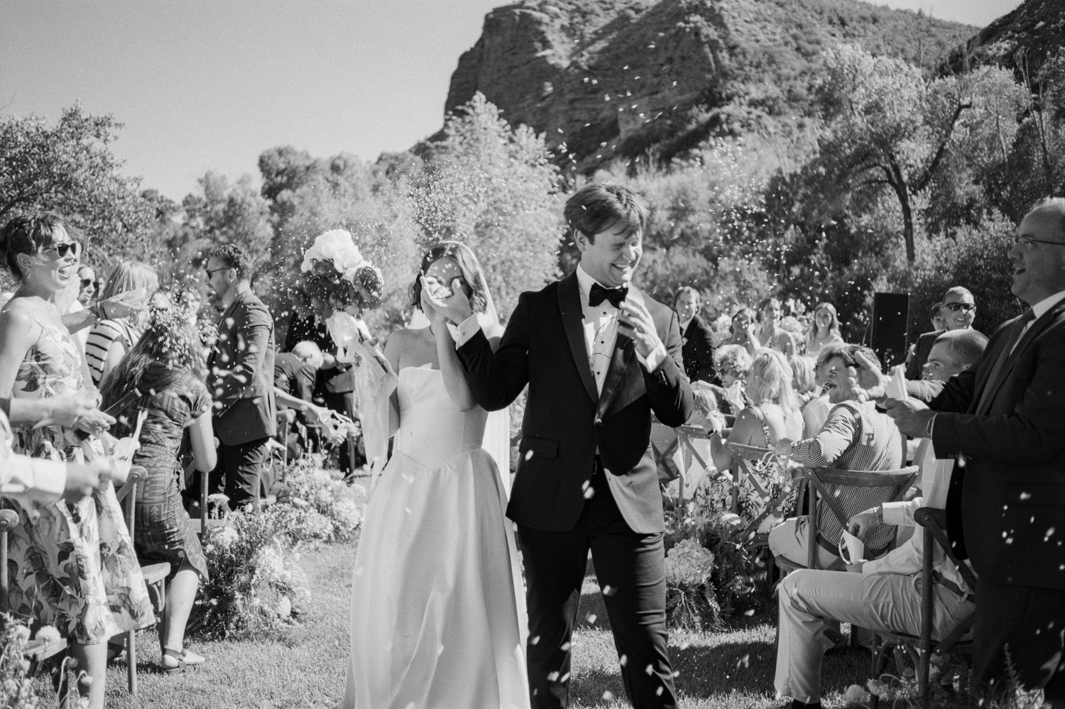 Wedding guests celebrate outdoors at a garden ceremony with joyful expressions and dancing.