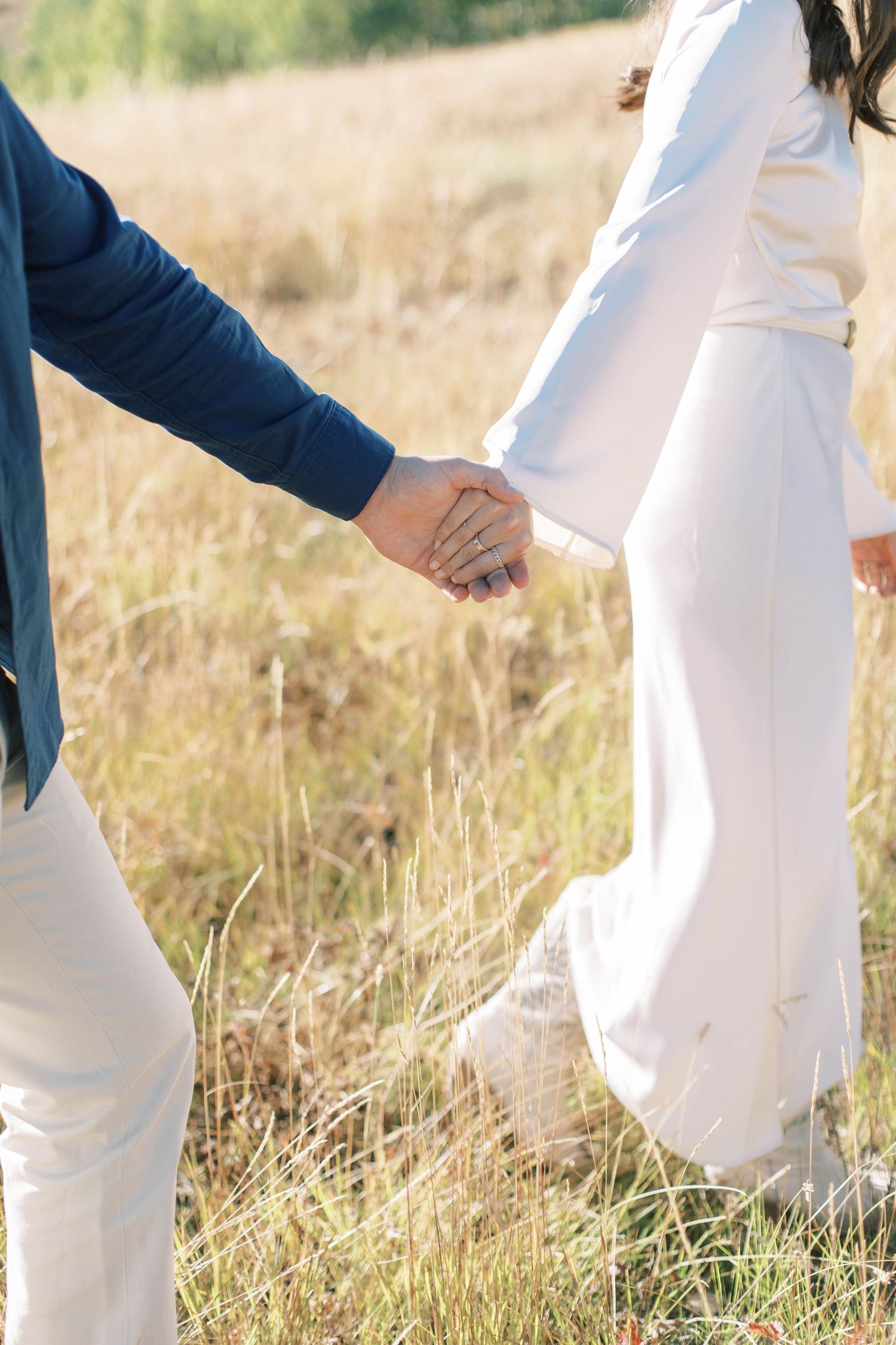 Detail shot of couple holding hands in flowing white and navy outfits against mountain backdrop.