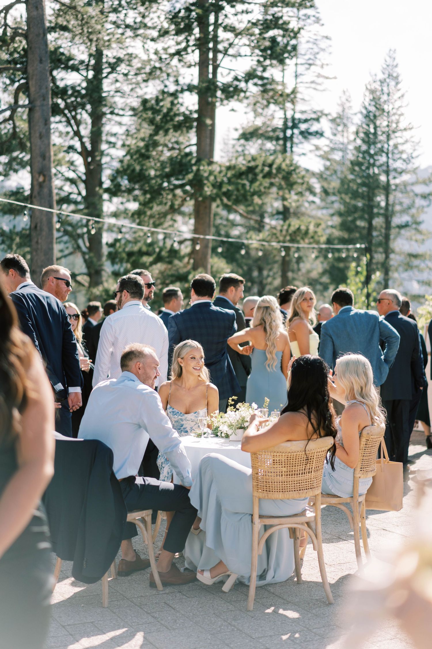 Outdoor mountain wedding reception with guests seated at tables among tall pine trees at everline resort in lake tahoe.