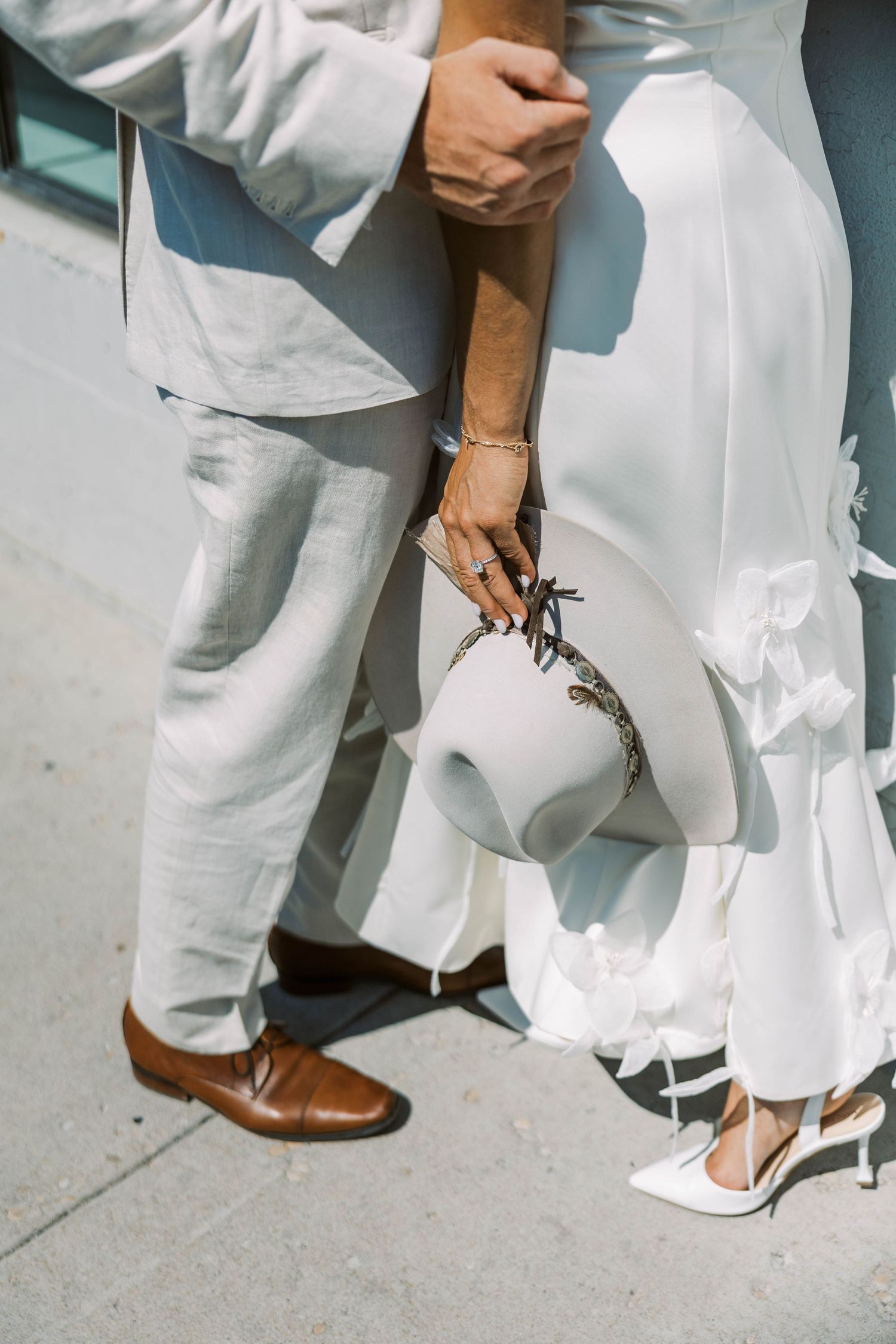 Contrasting footwear of wedding party members showing brown leather shoes and white bridal heels on concrete.
